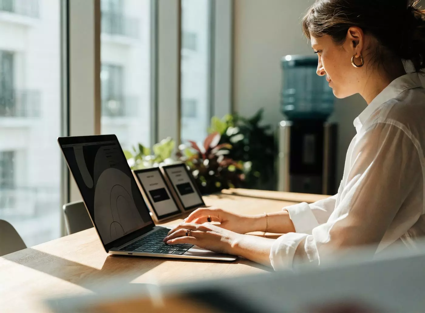 Collaboratrice mettant à jour ses contenus sur un ordinateur portable, deux petits écrans e-paper posés sur le bureau à côté d'elle