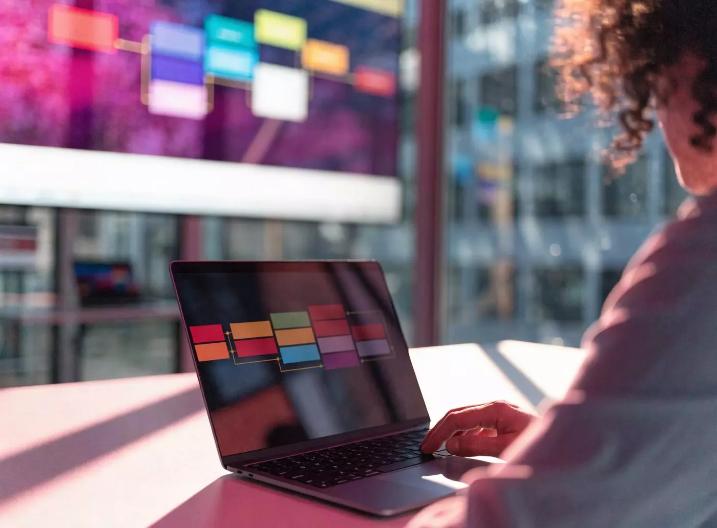 Communications manager planning a broadcast schedule on a laptop, wall screen in the background