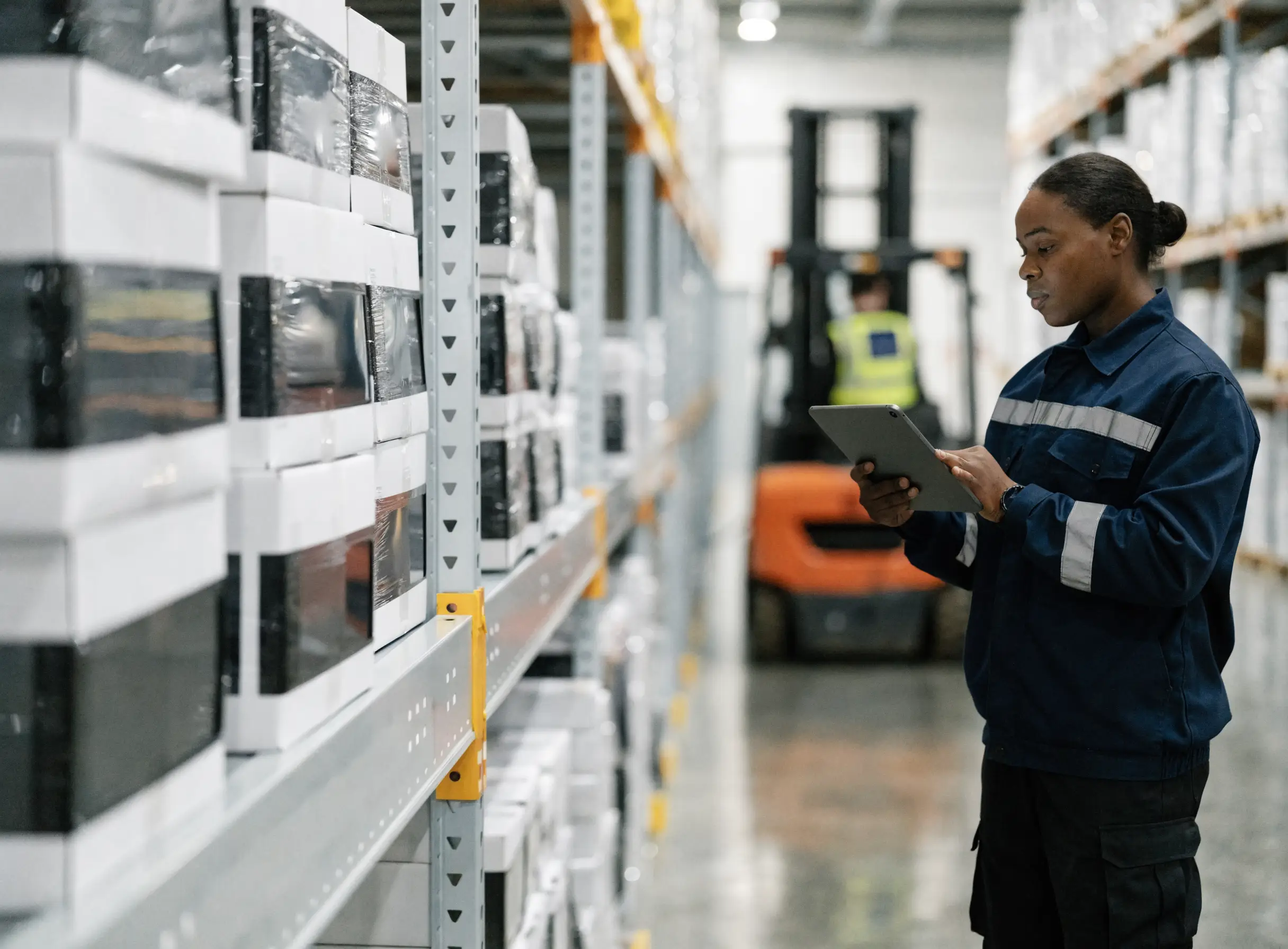 Warehouse manager, tablet in hand, between racks of boxed screens