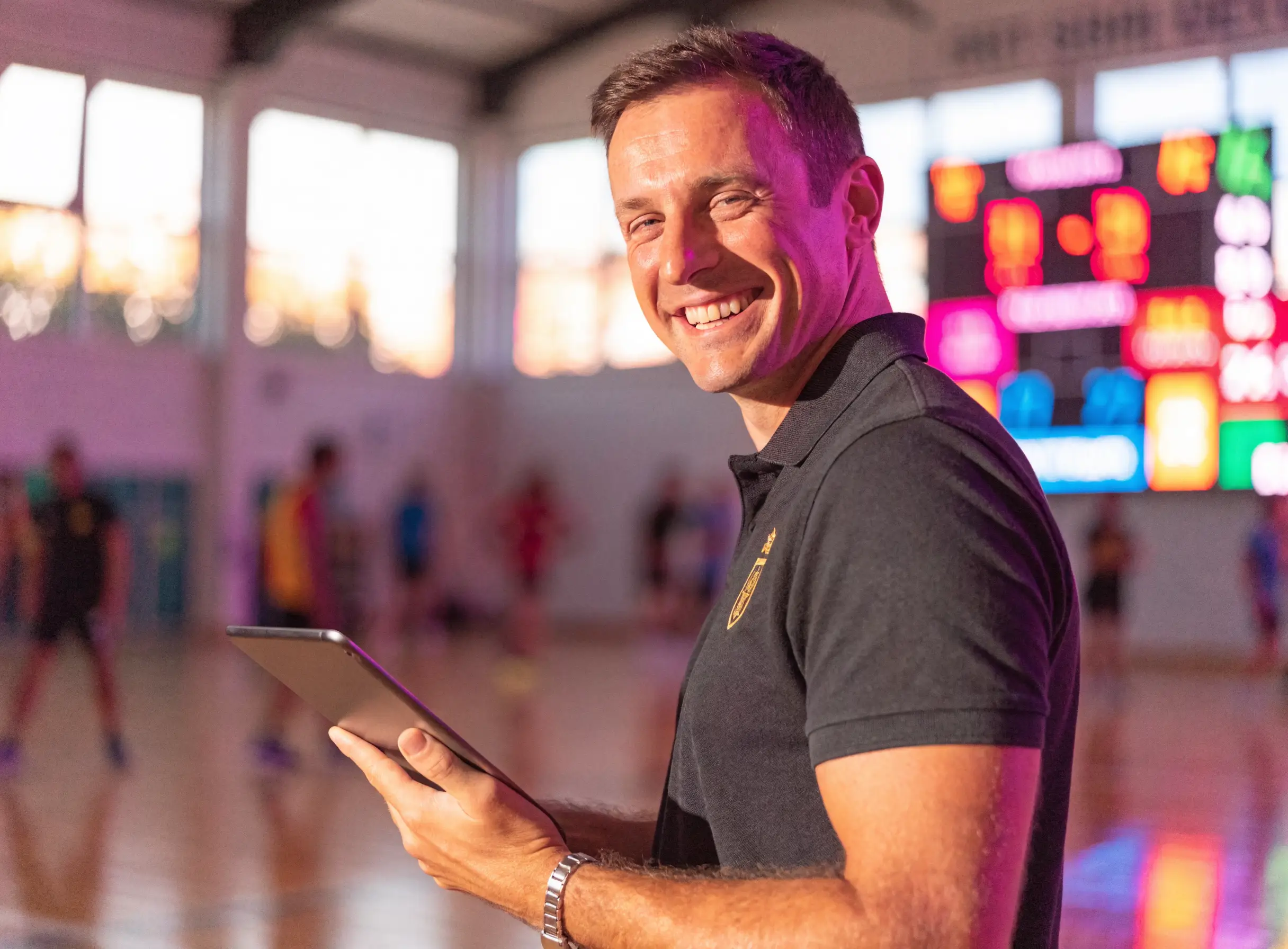Responsable de salle souriant configurant SCORING sur une tablette, tableau de score LED au-dessus