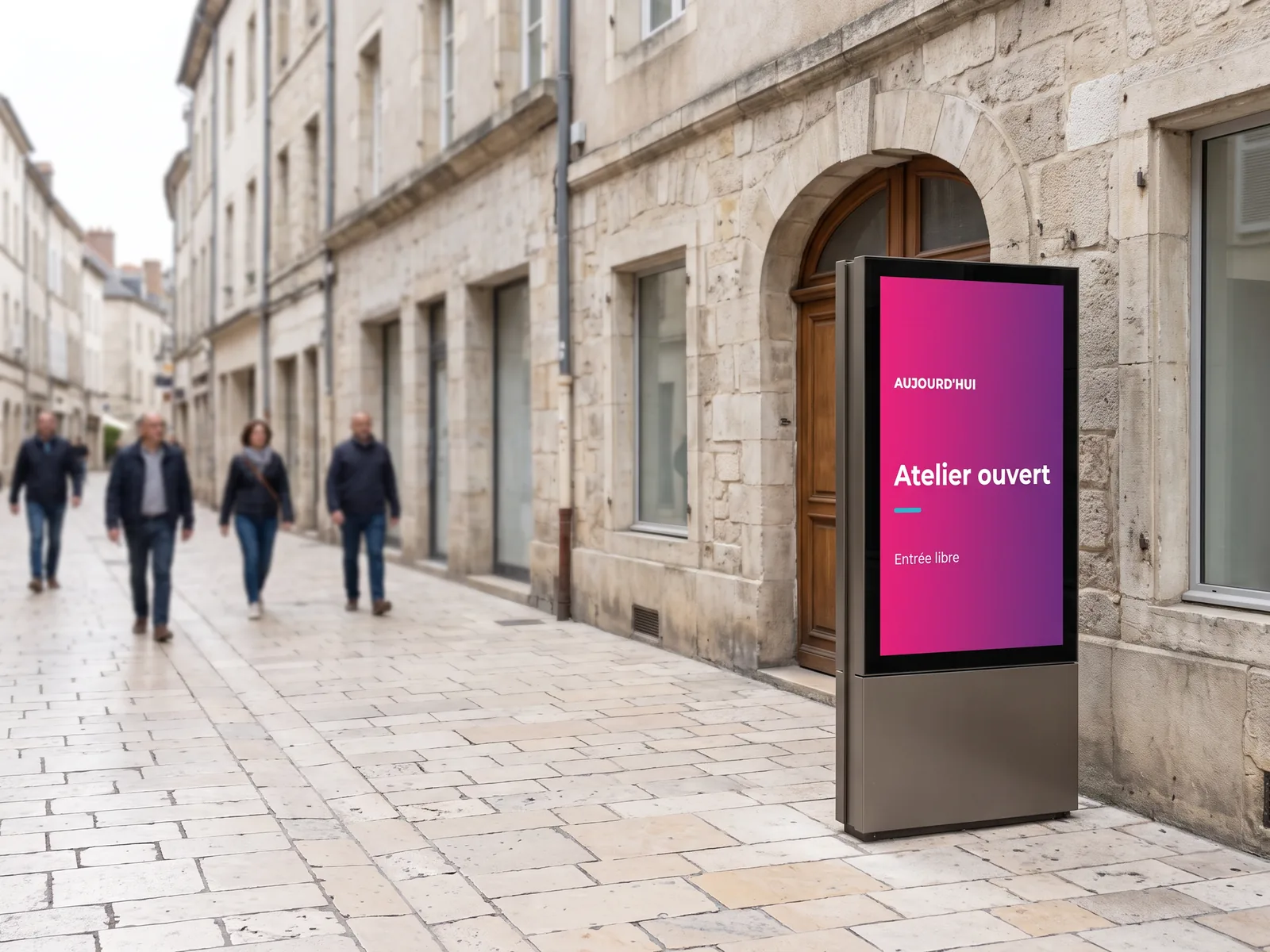 Totem num&eacute;rique ext&eacute;rieur pos&eacute; sur le trottoir d'une rue pi&eacute;tonne, annon&ccedil;ant un atelier ouvert