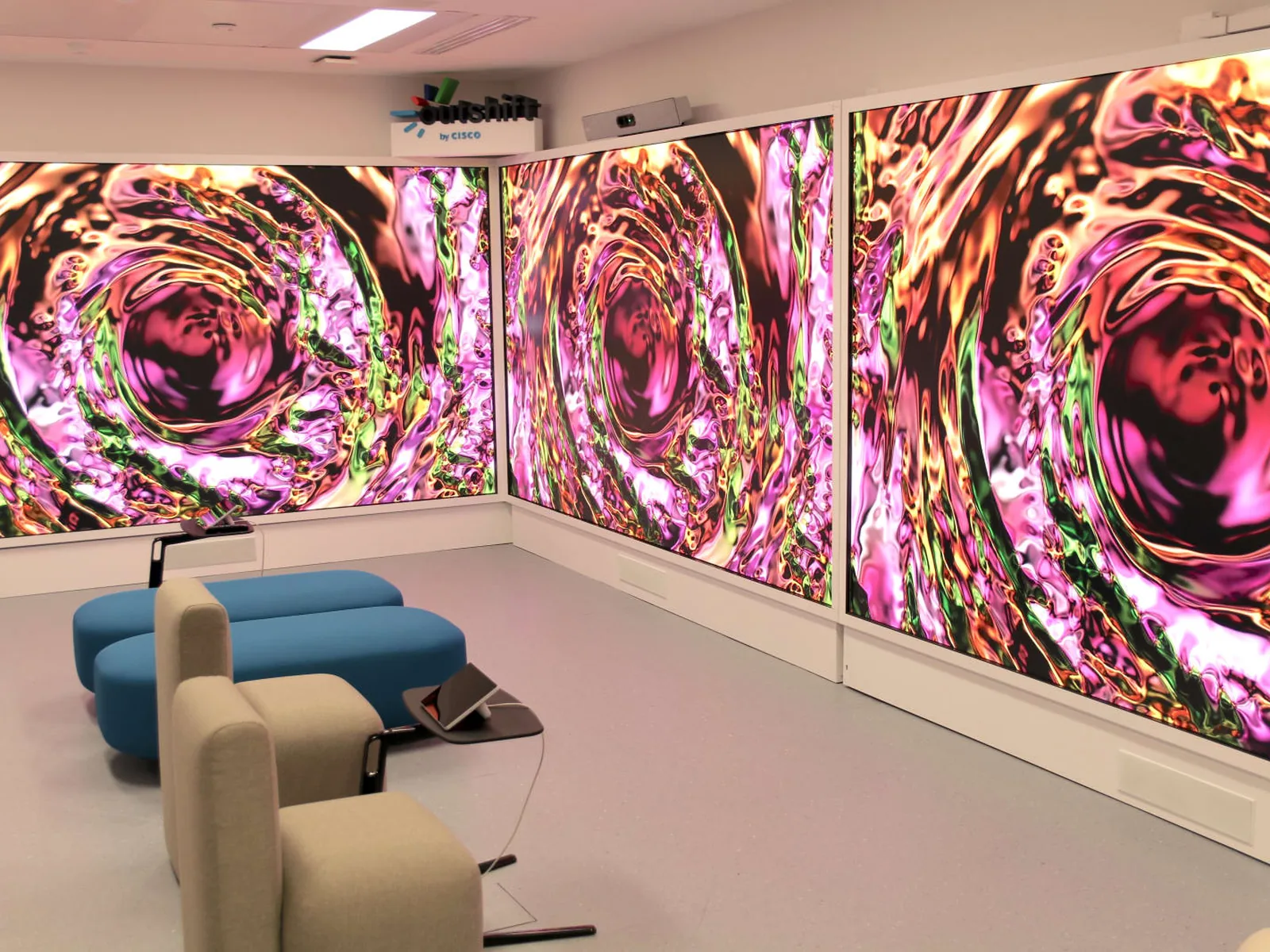 Salle de r&eacute;union dont les murs sont couverts d&rsquo;&eacute;crans LED diffusant une m&ecirc;me &oelig;uvre abstraite aux tons magenta