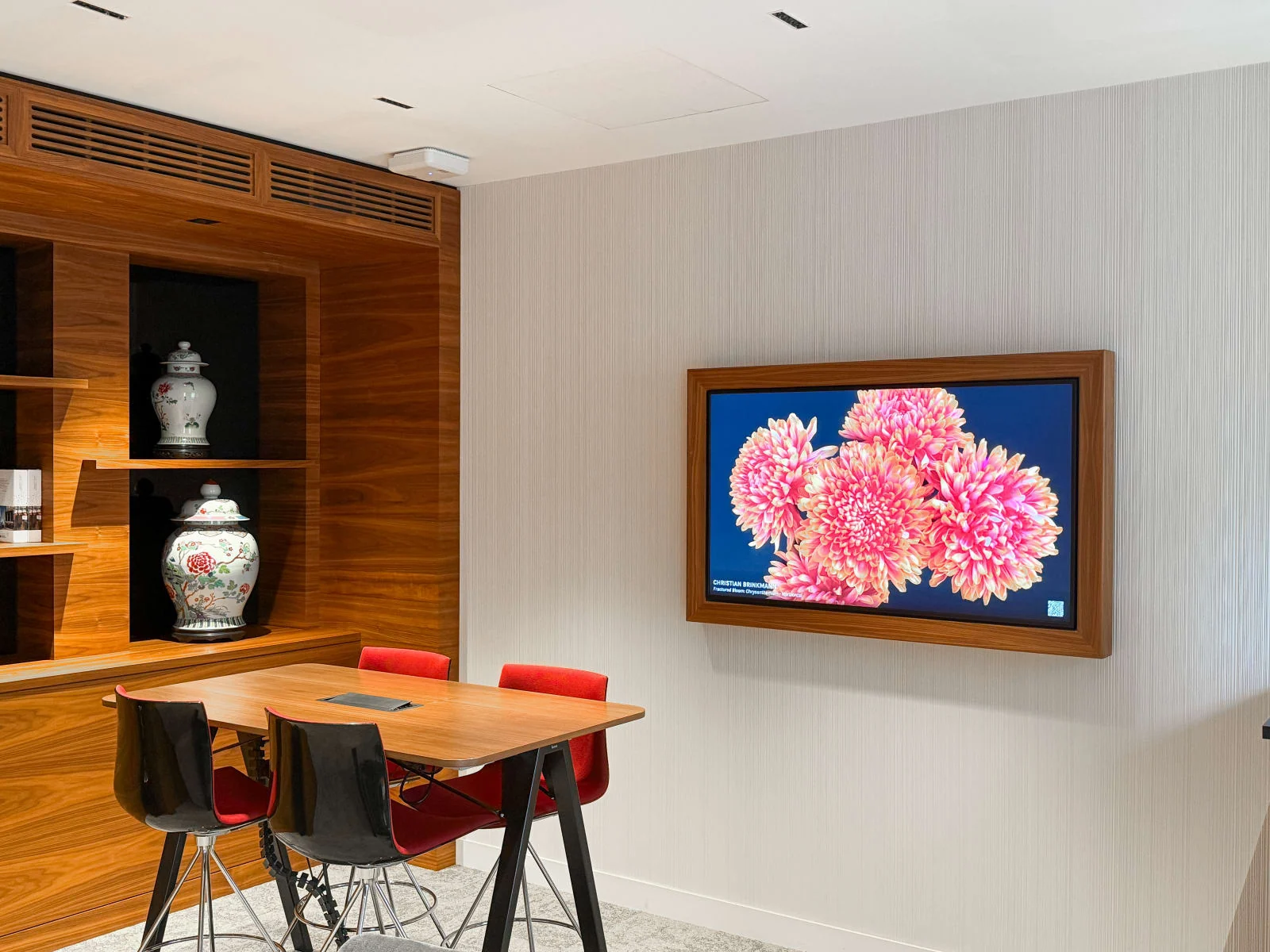 &Eacute;cran encadr&eacute; de bois diffusant une &oelig;uvre florale num&eacute;rique dans une salle de r&eacute;union, avec le nom de l&rsquo;artiste affich&eacute; en bas de l&rsquo;image