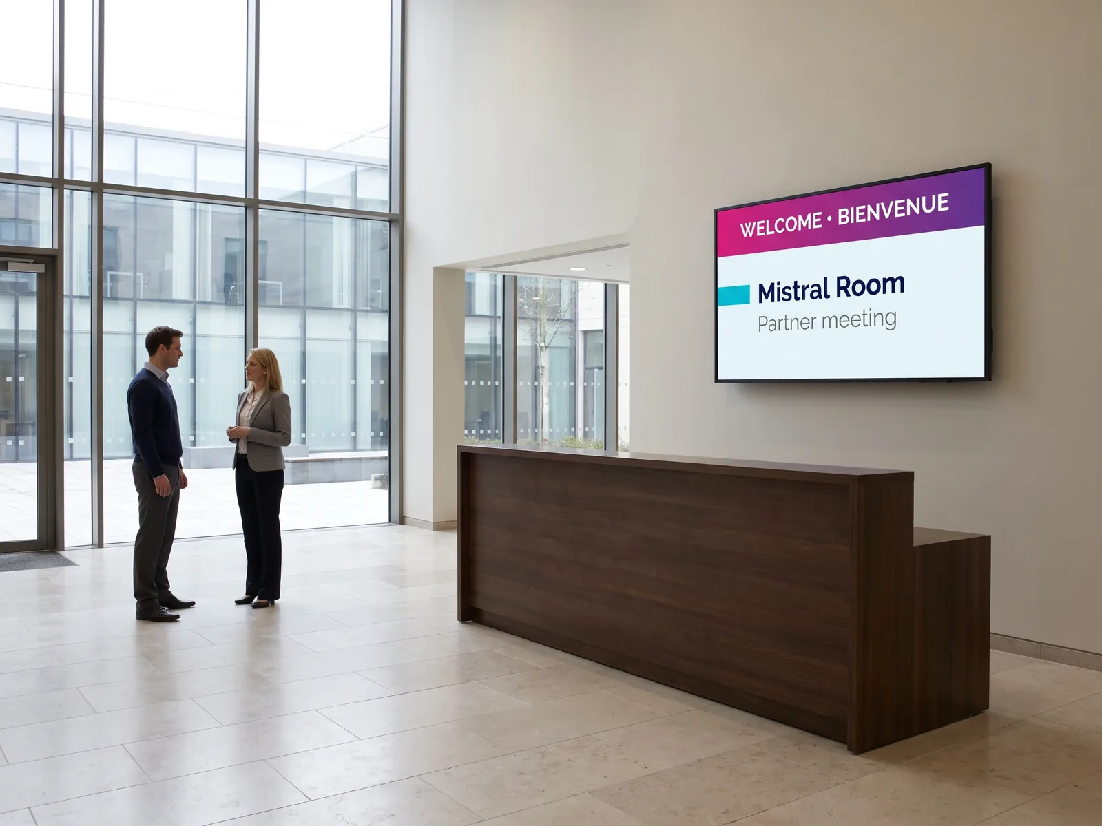 Wall-mounted screen in a conference centre reception showing a welcome message in English and French