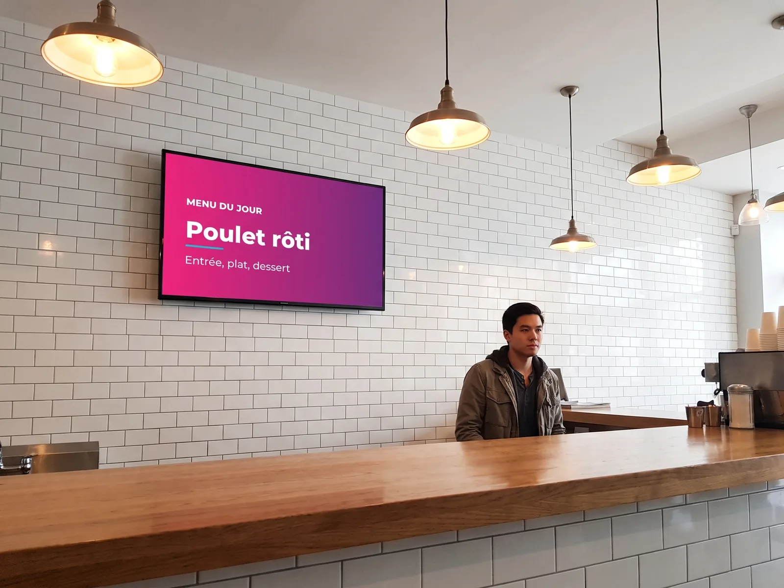 Écran mural derrière le comptoir d'un bistrot affichant le menu du jour