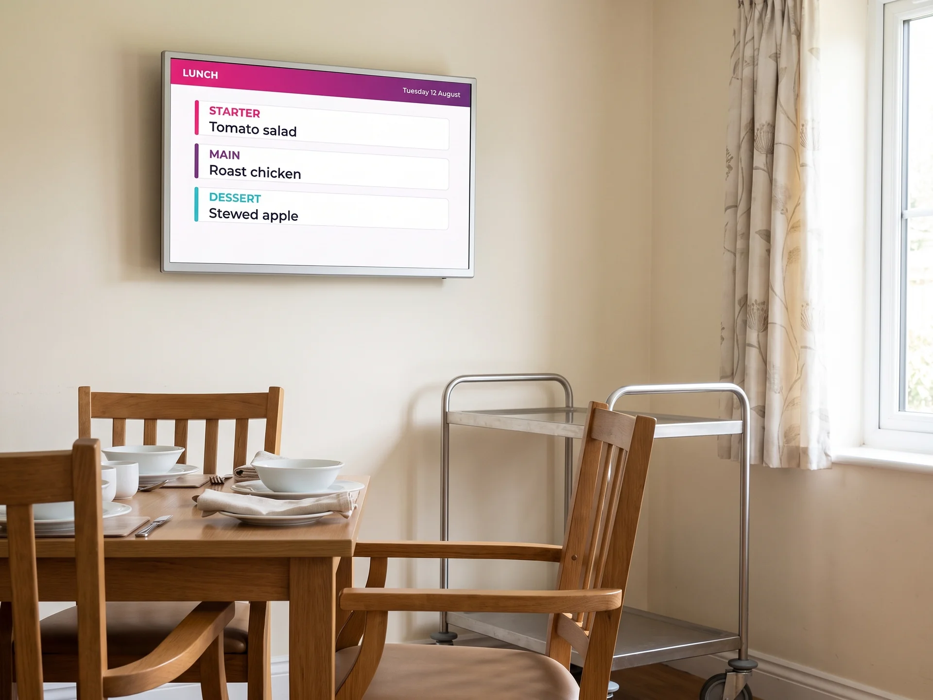 Table laid in a care home dining room below a screen showing the lunch menu