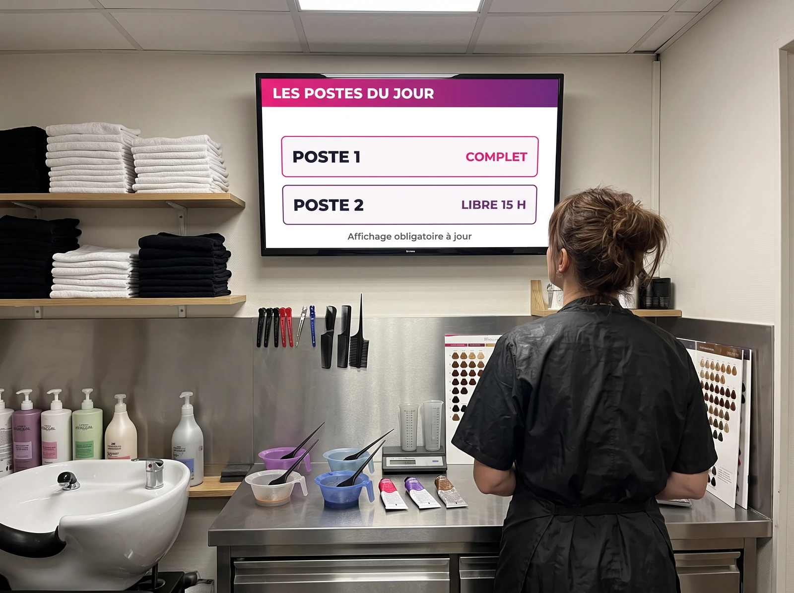 Coiffeuse devant un &eacute;cran affichant les postes du jour dans l&rsquo;arri&egrave;re-boutique d&rsquo;un salon