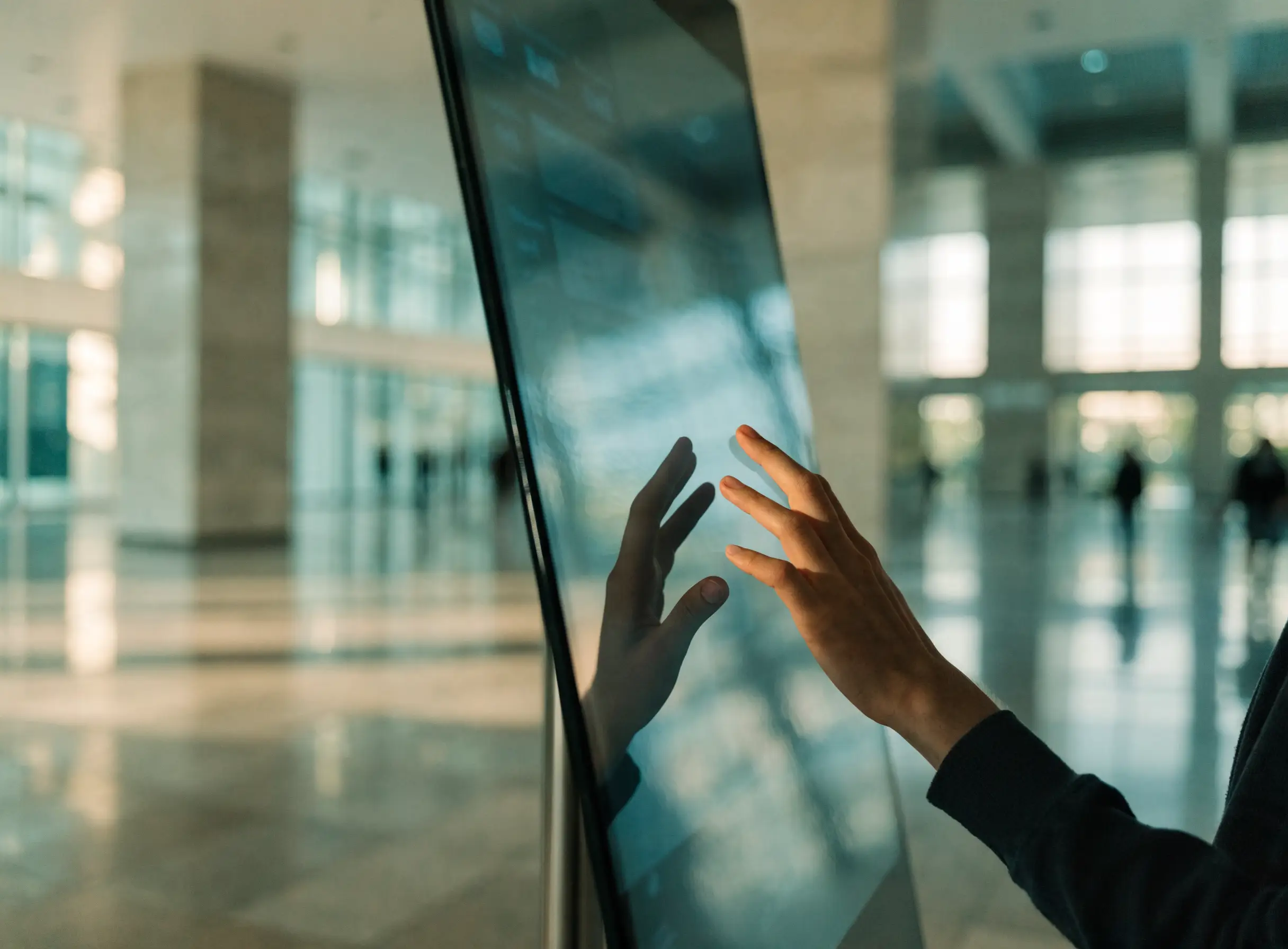 Main en contact avec une borne tactile verticale dans un hall