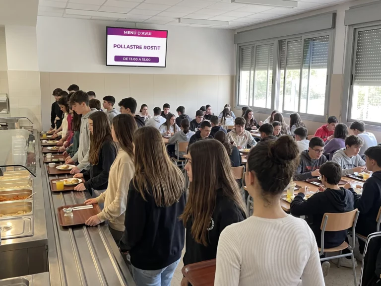 Pantalla sobre la barra de servei del menjador d'un centre educatiu mostrant el plat principal del dia i els torns