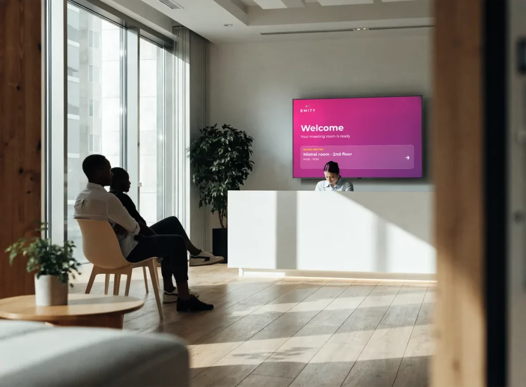 Welcome screen behind a reception desk showing a room and floor to two waiting guests