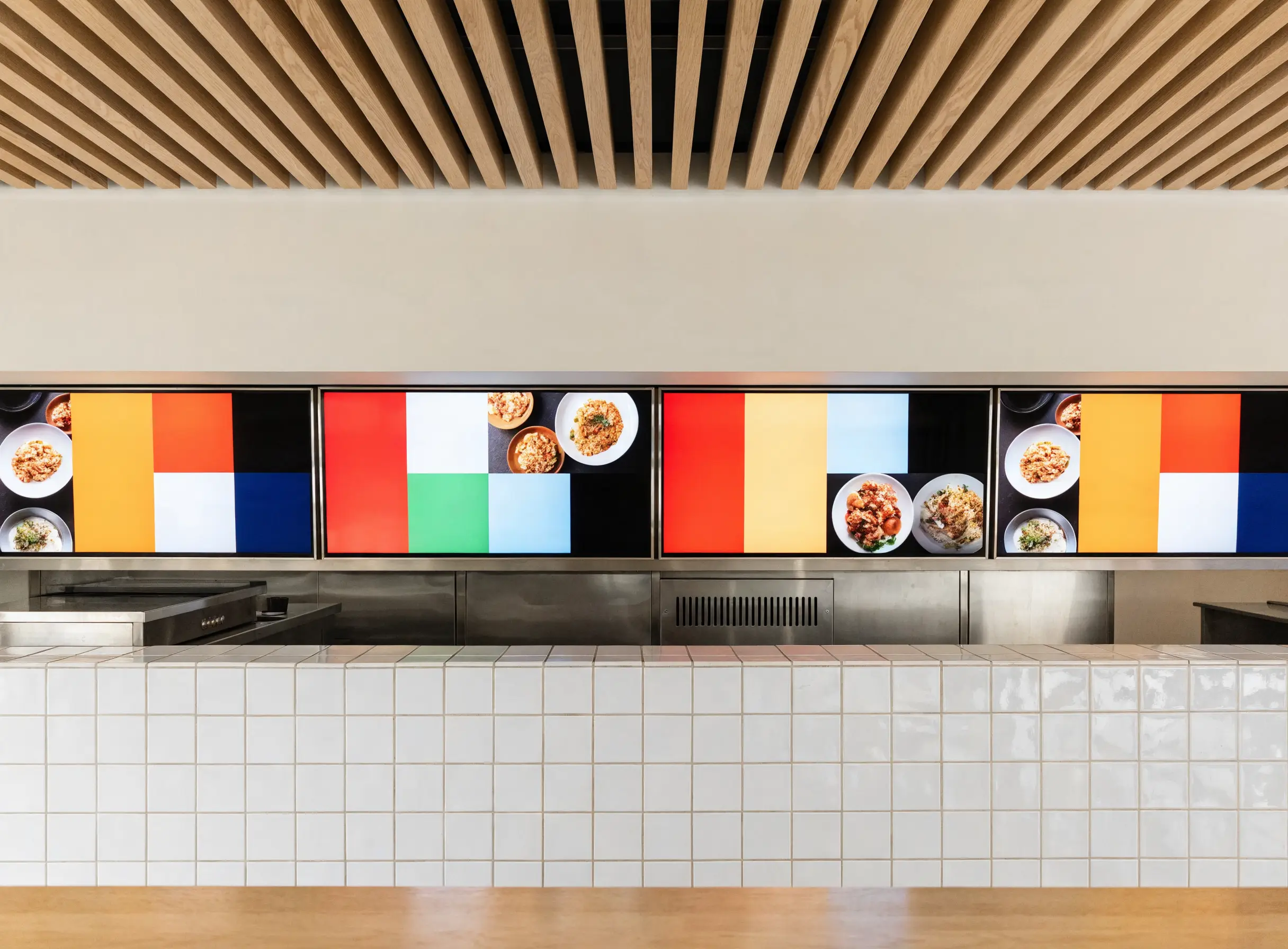 Quatre écrans alignés au-dessus du comptoir d'un restaurant, affichant les menus