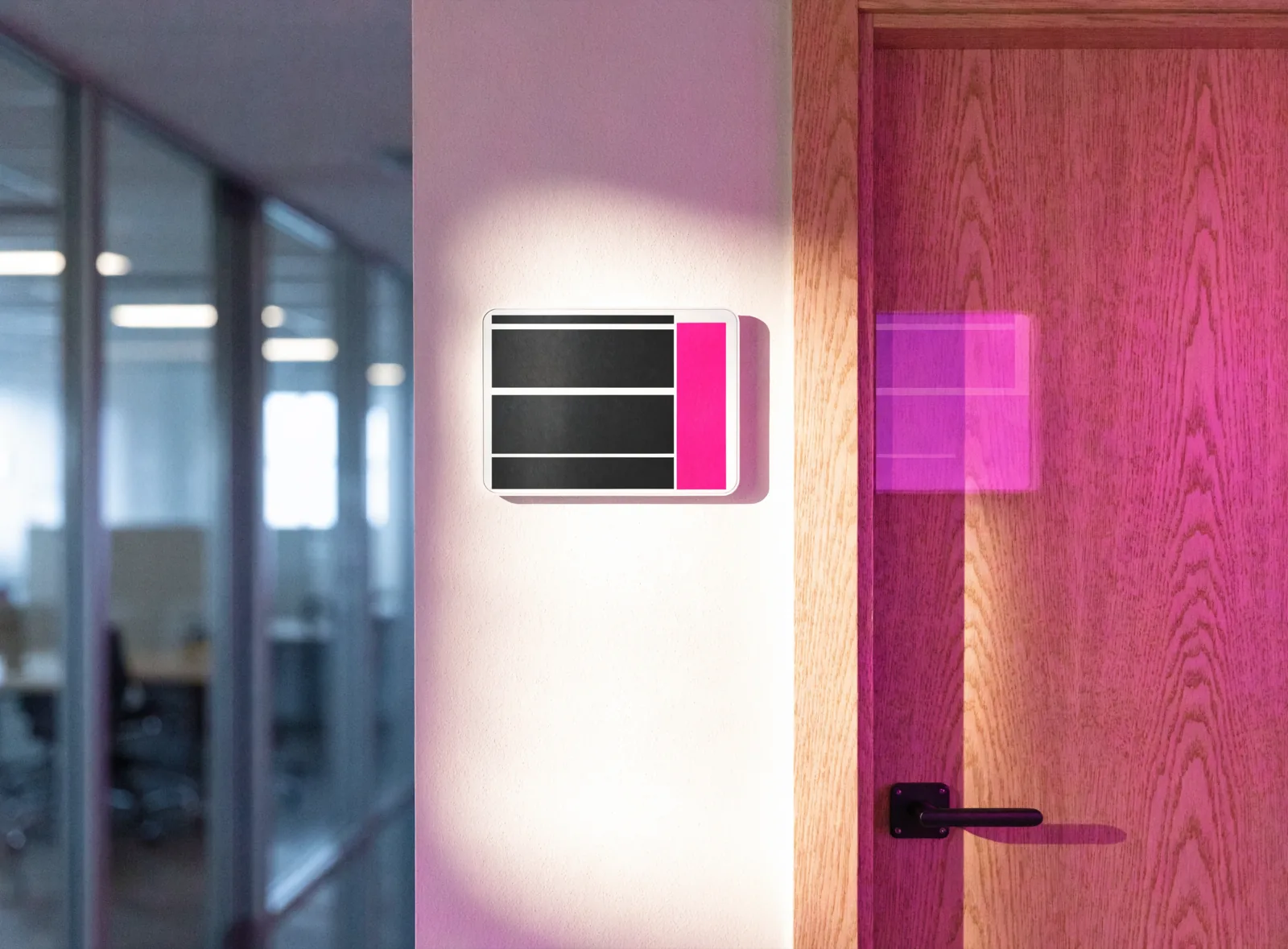 Small wireless e-paper sign mounted on the wall beside a meeting room door