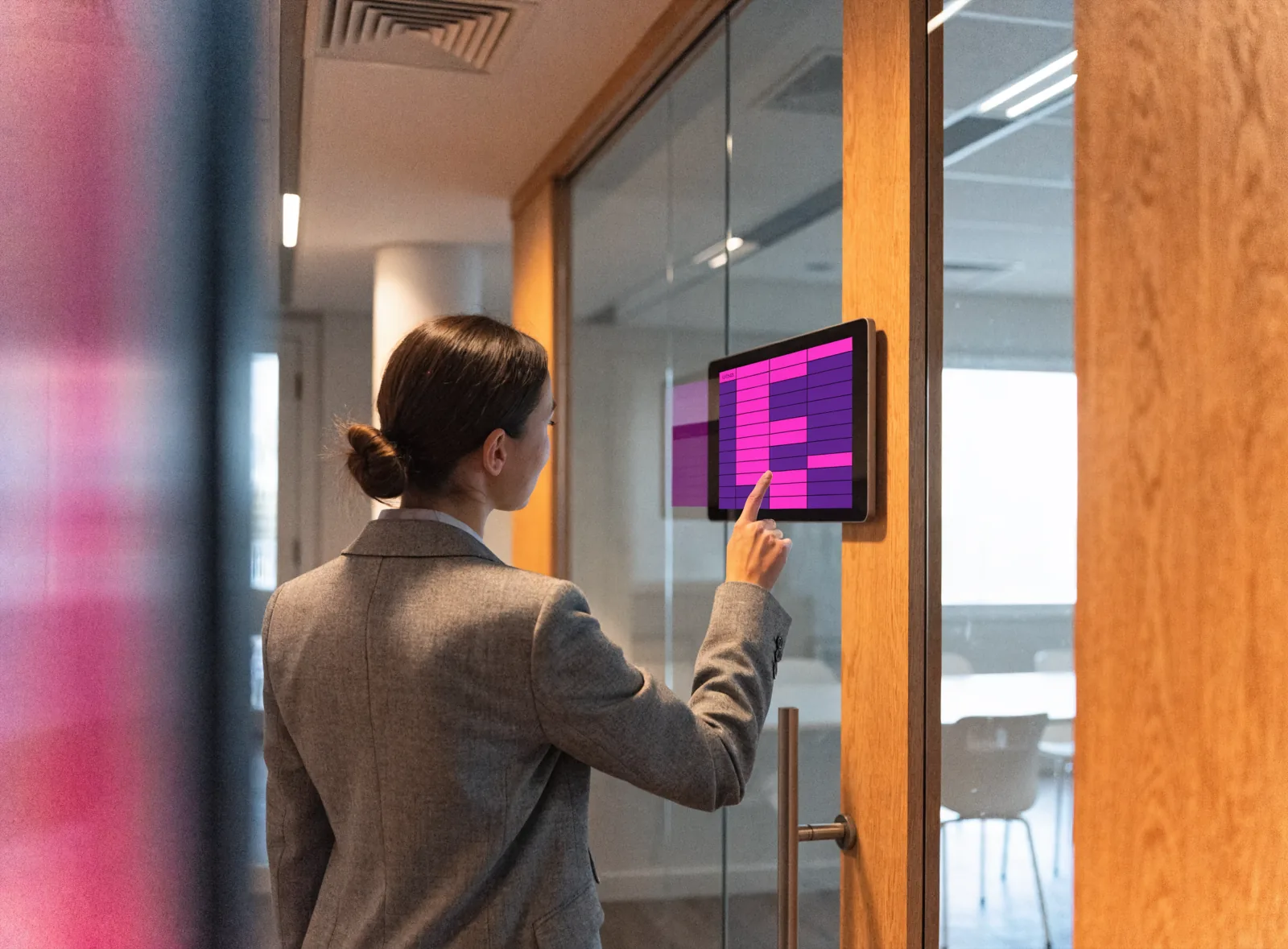 Employee checking the room-booking touch screen mounted beside a glass meeting room door