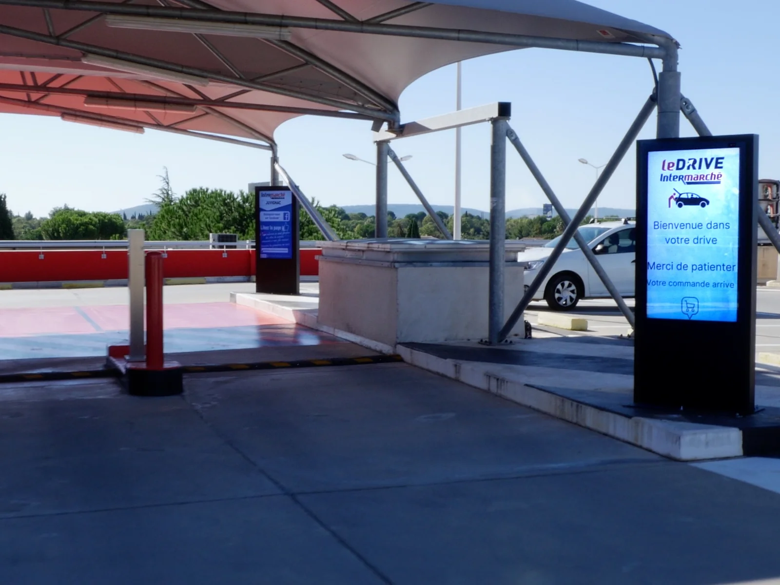 Totem d'affichage dynamique extérieur au drive d'un supermarché, affichant l'avancement de la commande