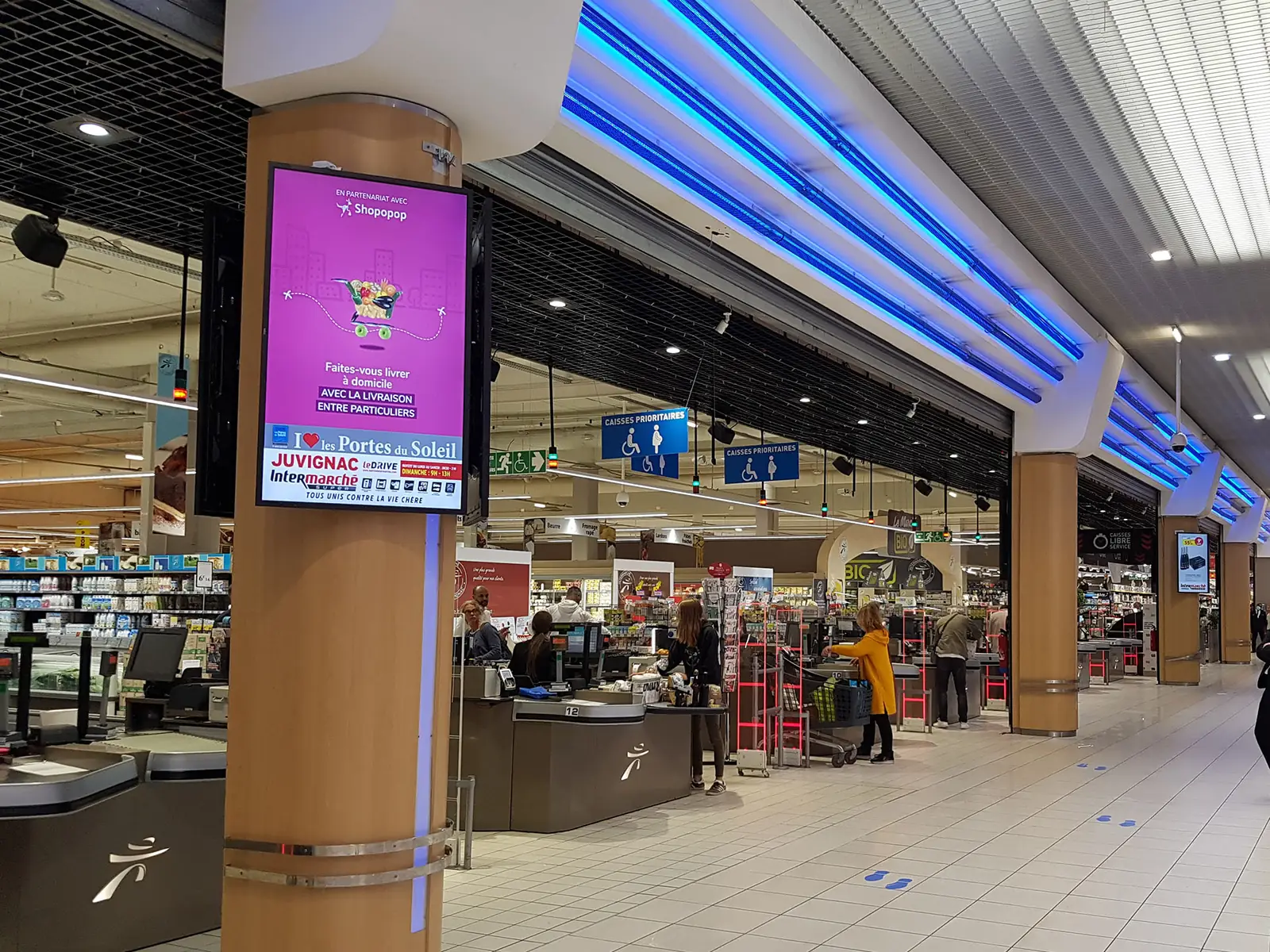 Totem d'affichage dynamique sur une colonne, face à la ligne de caisses d'un supermarché