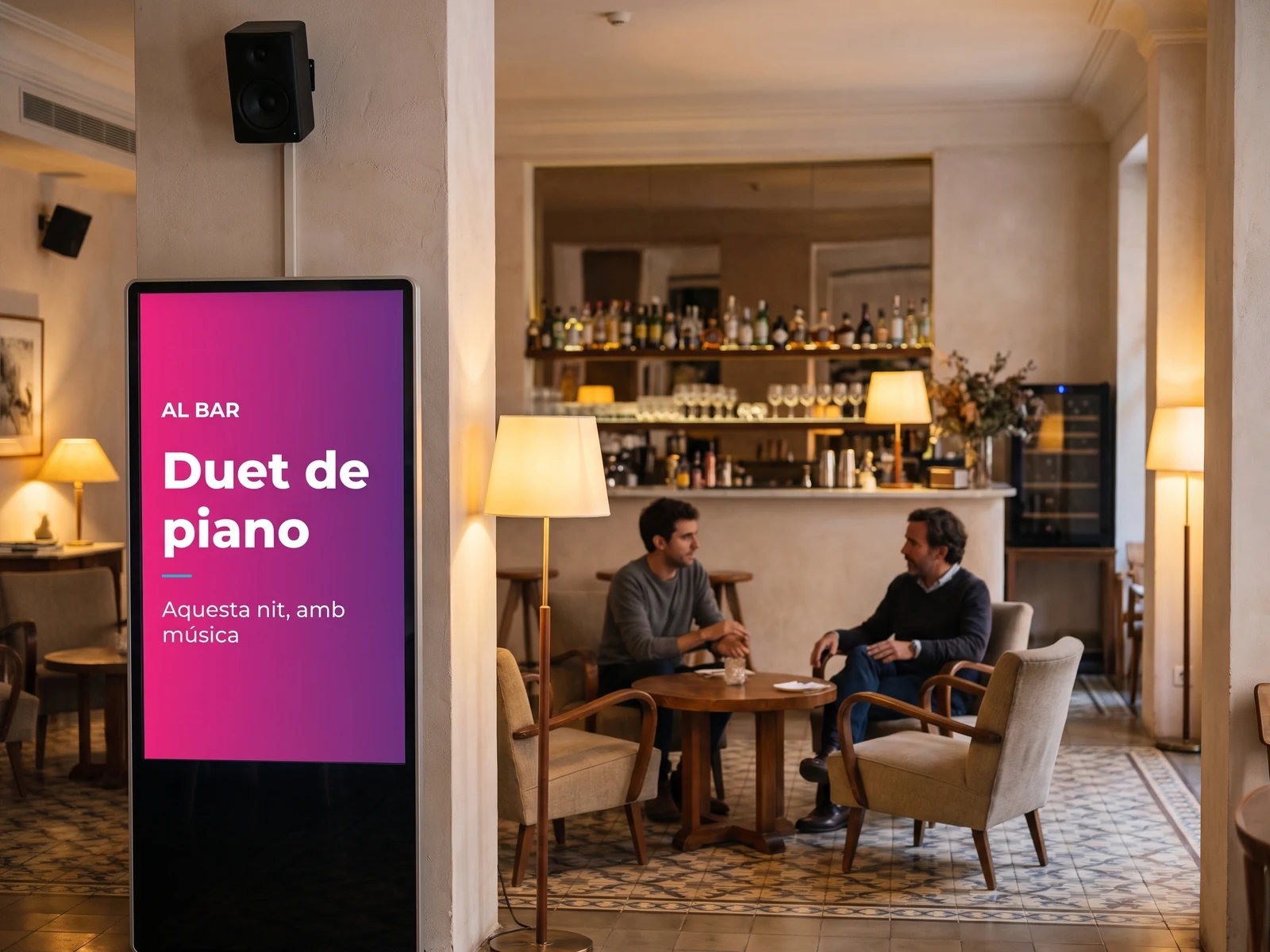 Pantalla vertical al bar d'un hotel anunciant la vetllada, amb un altaveu mural a sobre