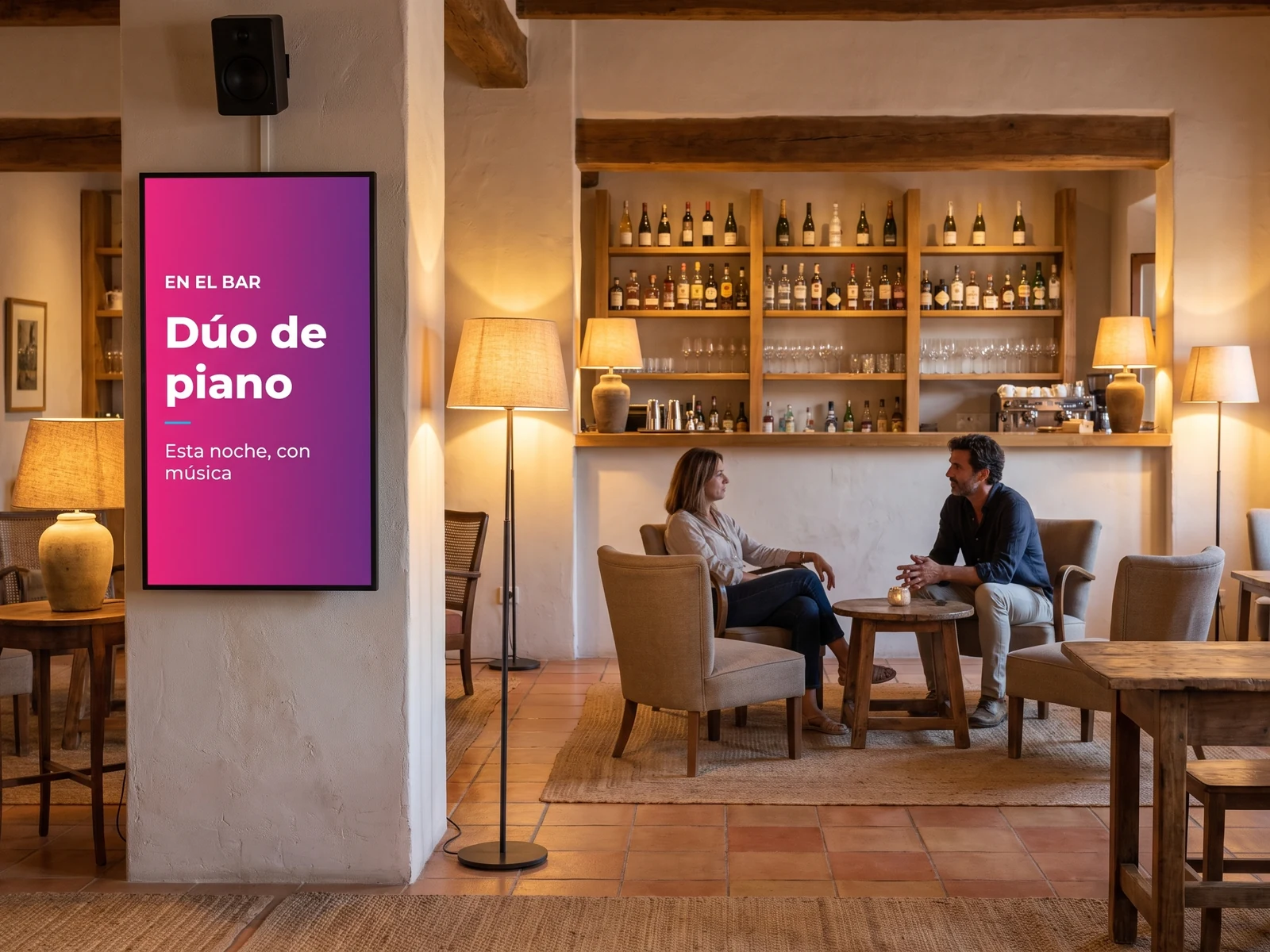 Pantalla vertical en la pared del bar de un hotel anunciando la velada, con un altavoz mural encima