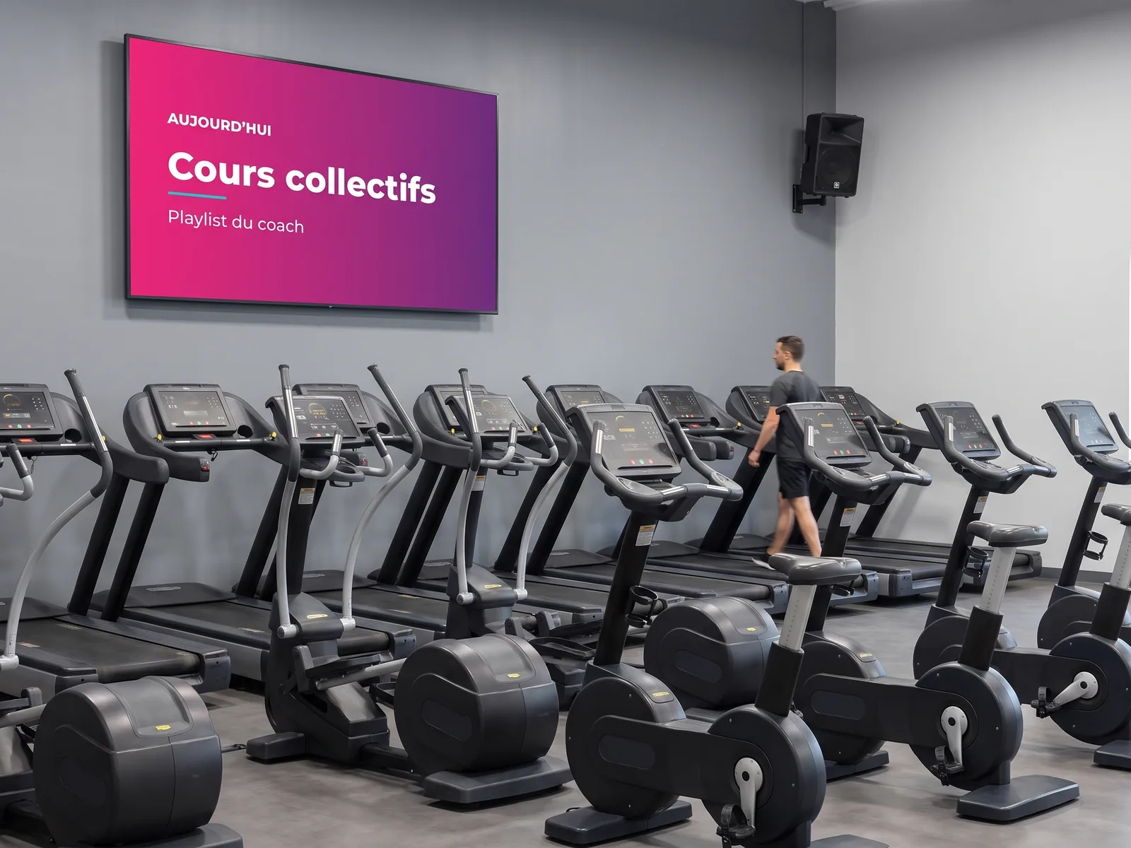 Écran mural annonçant les cours collectifs dans une salle de sport, avec une enceinte fixée au mur