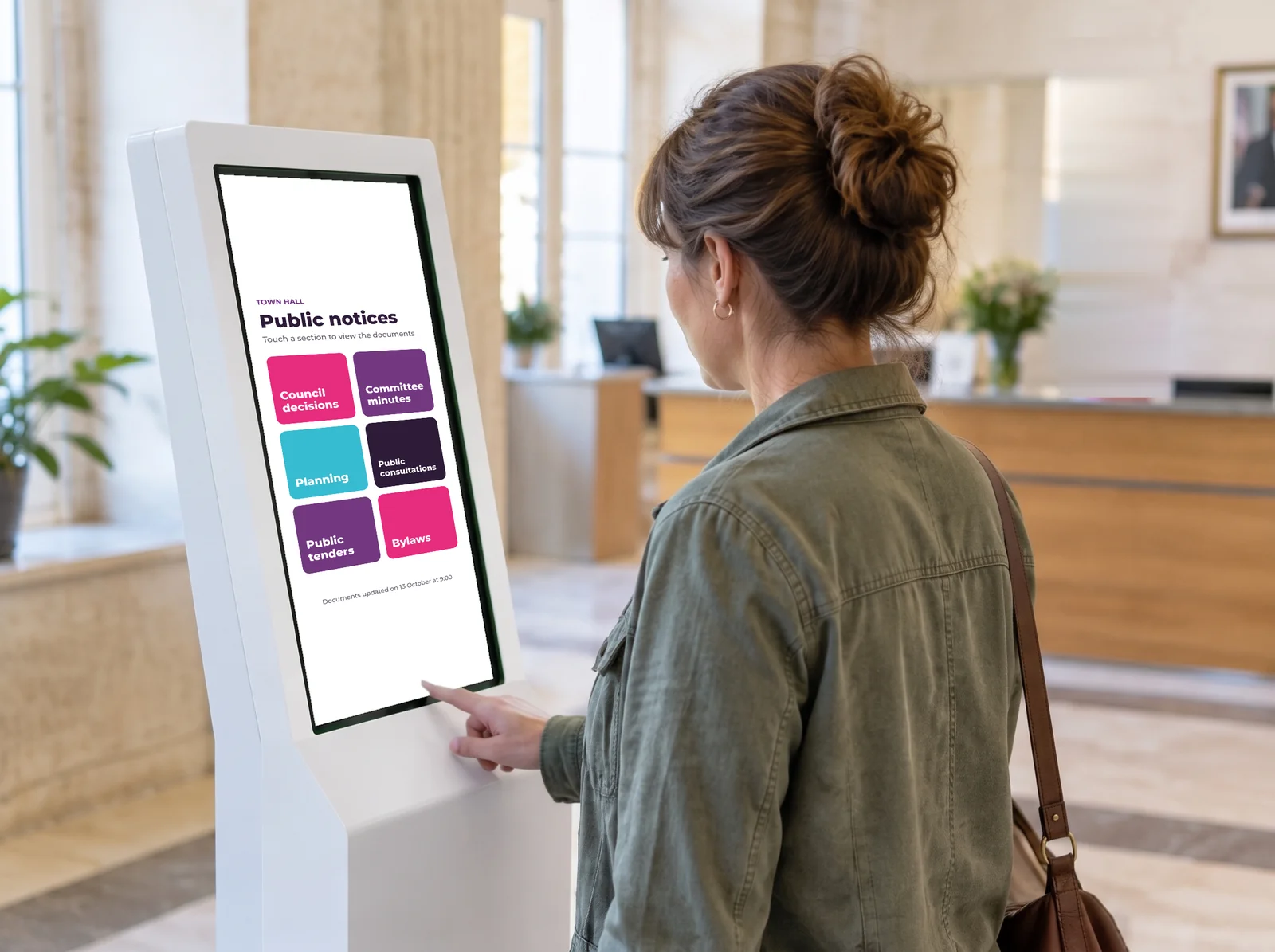 Resident reading council notices on a touchscreen kiosk in a town hall foyer