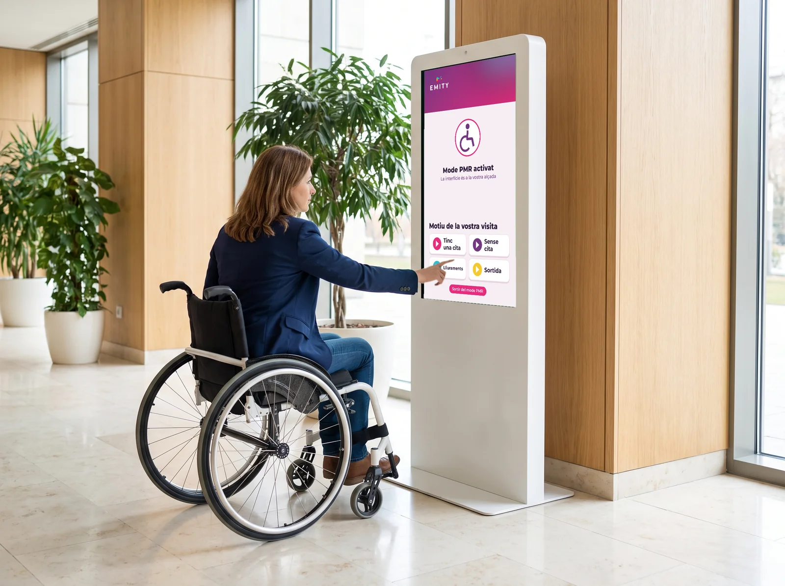 Persona en cadira de rodes que fa servir un quiosc tàctil amb la interfície abaixada en mode accessible