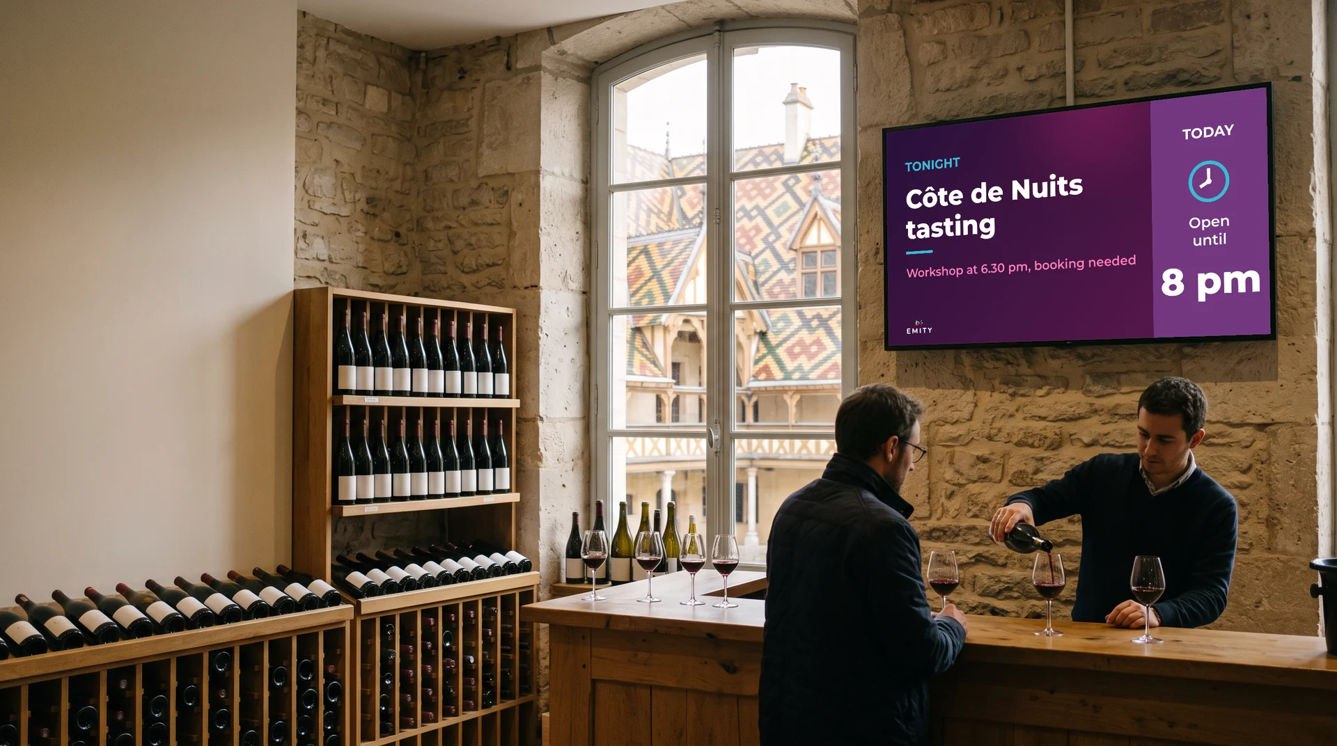 Wine bar with stone walls, glazed tile roofs through the window: a wine merchant pours a glass under the screen reading “Côte de Nuits tasting”