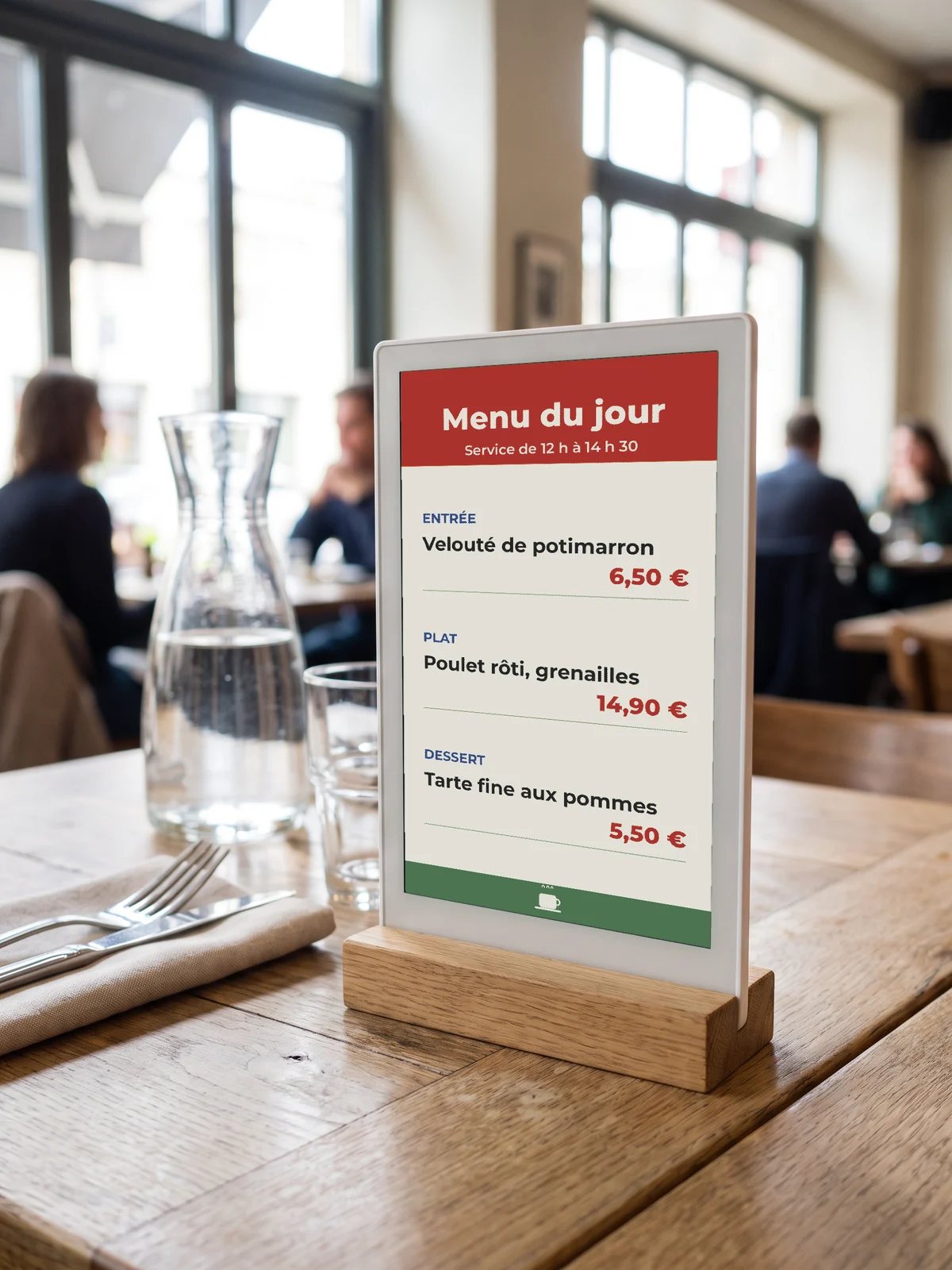 Chevalet e-paper « Menu du jour » dans un cadre blanc sur socle en chêne, posé sur une table de bistrot près d'une carafe d'eau