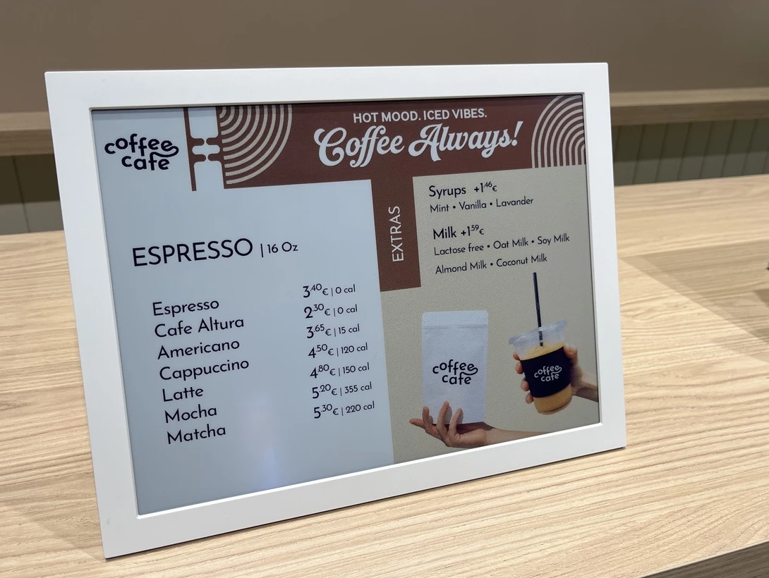 Écran e-paper Samsung à cadre blanc posé sur le comptoir d'un café, affichant la carte des boissons en couleur