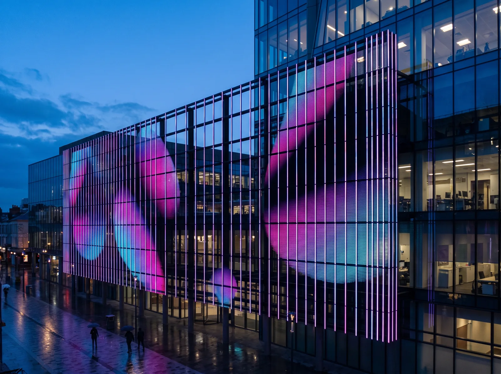 Maille LED à larges ajours sur la façade vitrée d'un immeuble, à la nuit tombante