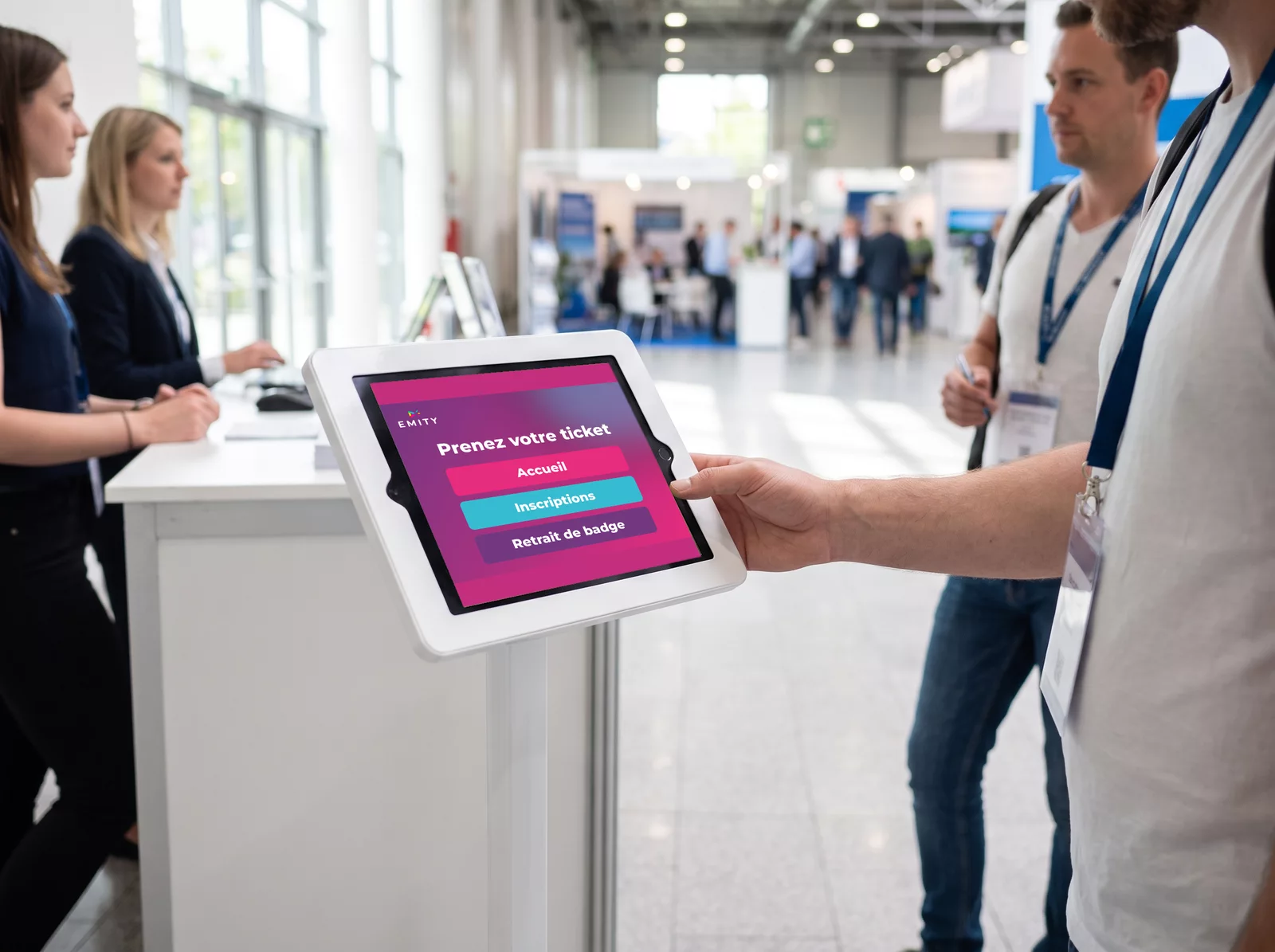 Visiteur qui prend son ticket sur une tablette d'accueil « Prenez votre ticket »
