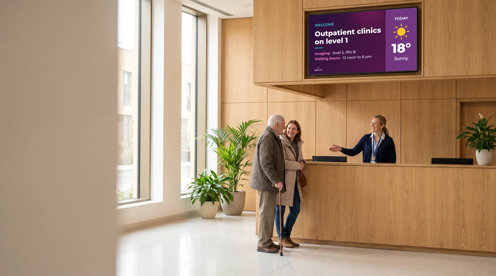 Hospital reception: an elderly man and his daughter helped by the receptionist, under the outpatients screen
