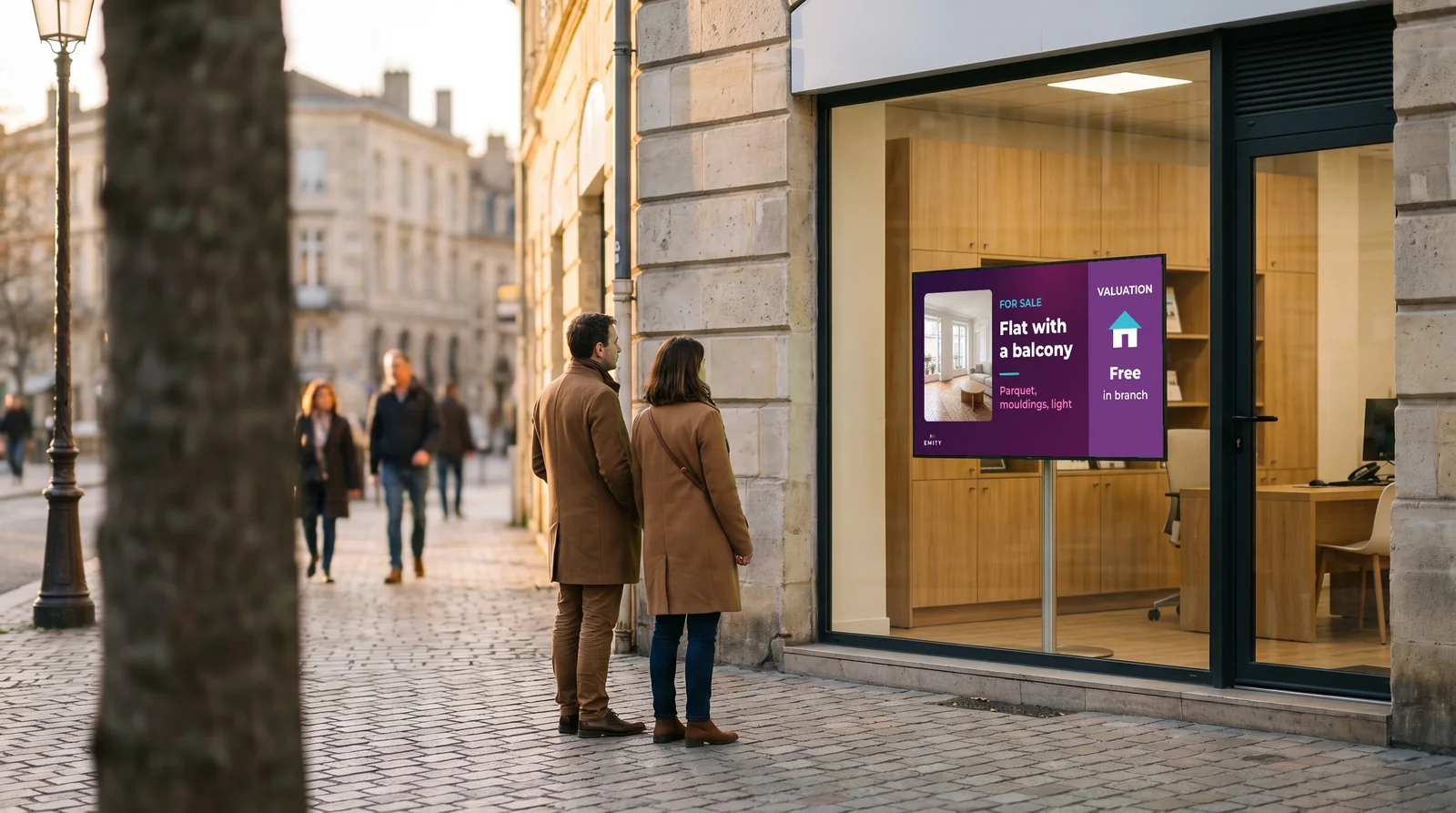 Couple stopping at an estate agency window: the screen shows a flat with a balcony for sale and a free valuation in branch