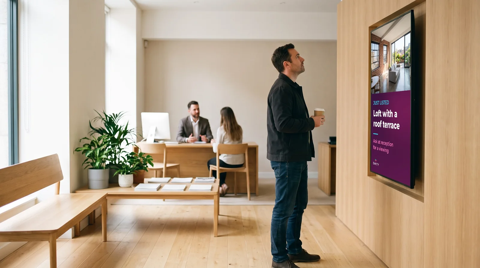 Client in an estate agency waiting area reading a portrait screen that presents a loft with a roof terrace