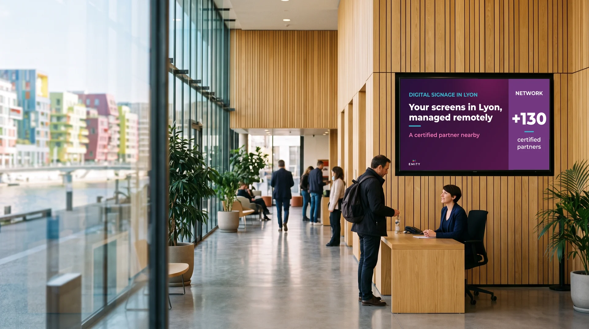 Office building lobby in Confluence: at the desk, under the screen “Your screens in Lyon, managed remotely”, a receptionist welcomes a visitor