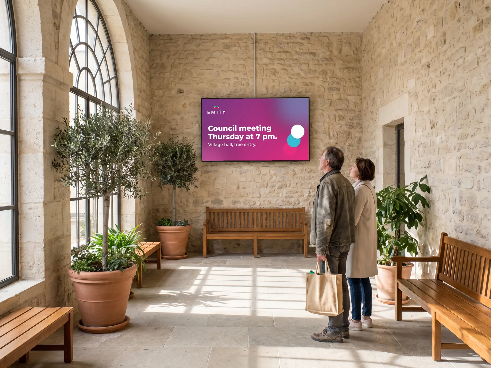Town hall lobby: two residents read the council meeting notice on the wall screen