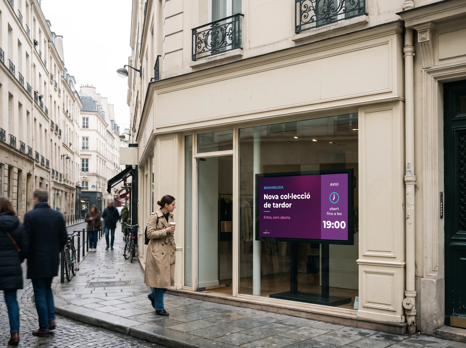Carrer de París al matí: una vianant amb un cafè mira la pantalla de l'aparador d'una botiga haussmanniana «Benvinguda · Nova col·lecció de tardor»