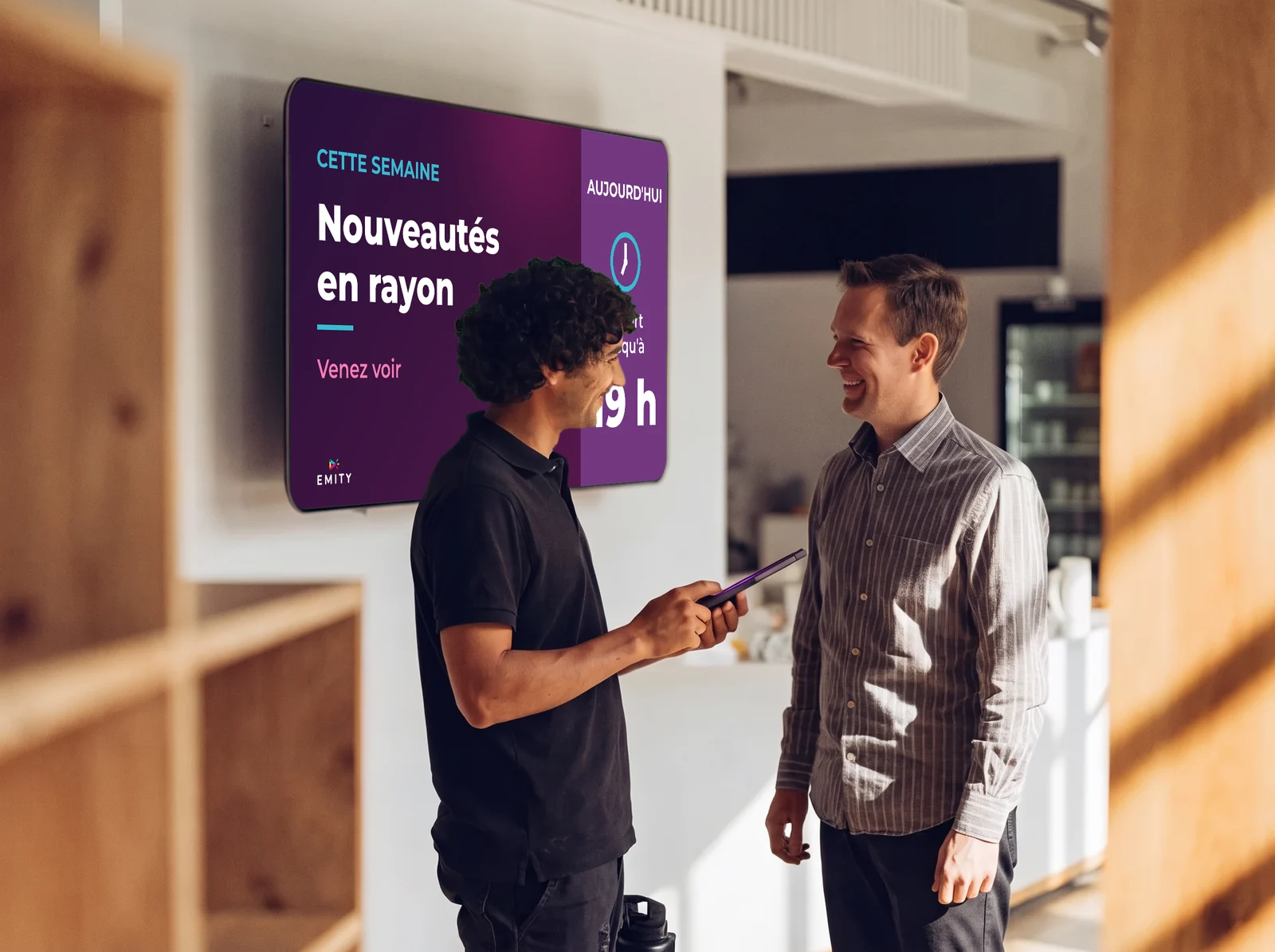 Technicien d'un revendeur certifié, tablette en main, qui échange avec son client devant l'écran du magasin « Nouveautés en rayon »