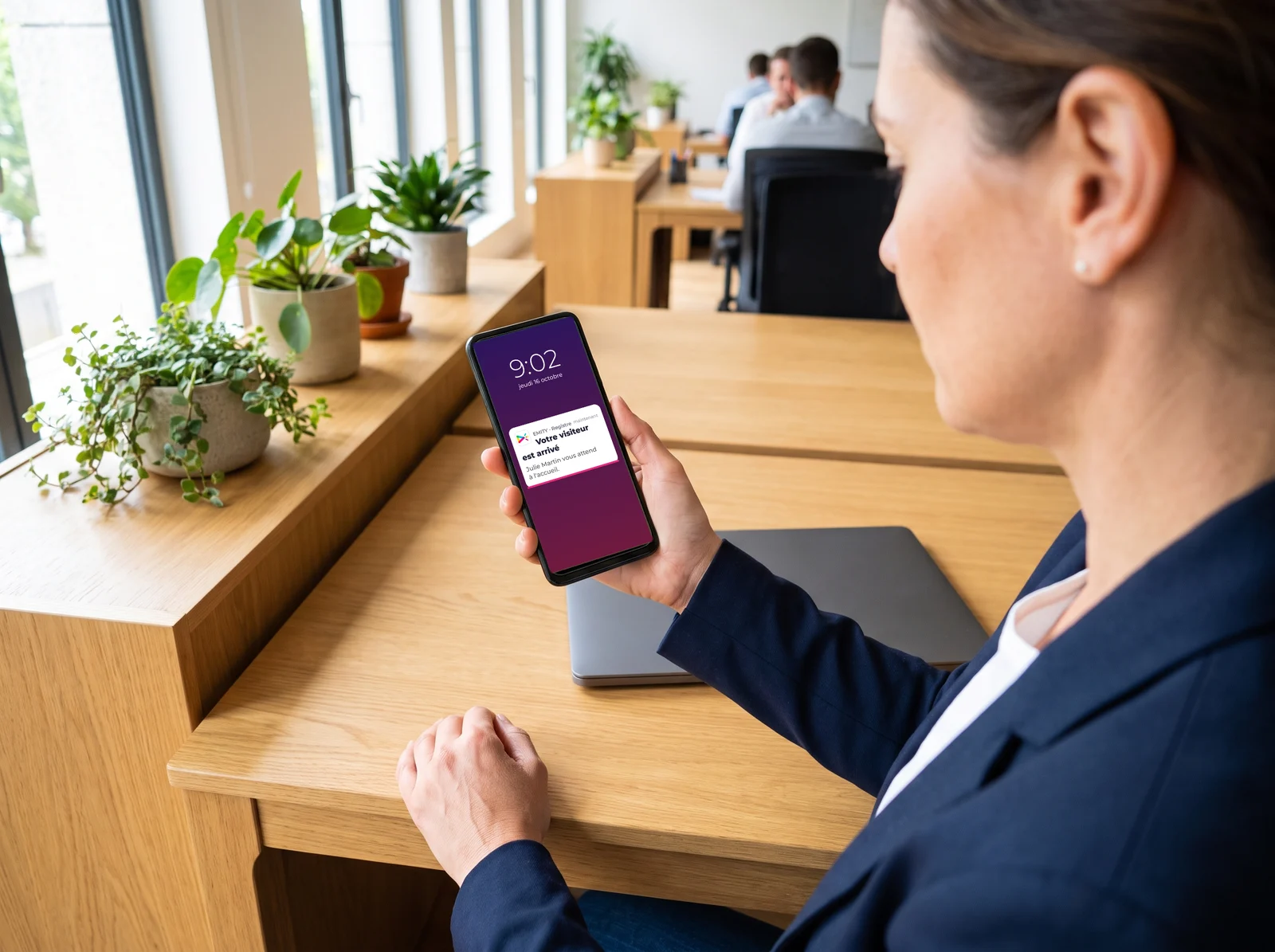 Collaboratrice à son bureau qui lit sur son téléphone la notification « Votre visiteur est arrivé » envoyée par le registre EMITY