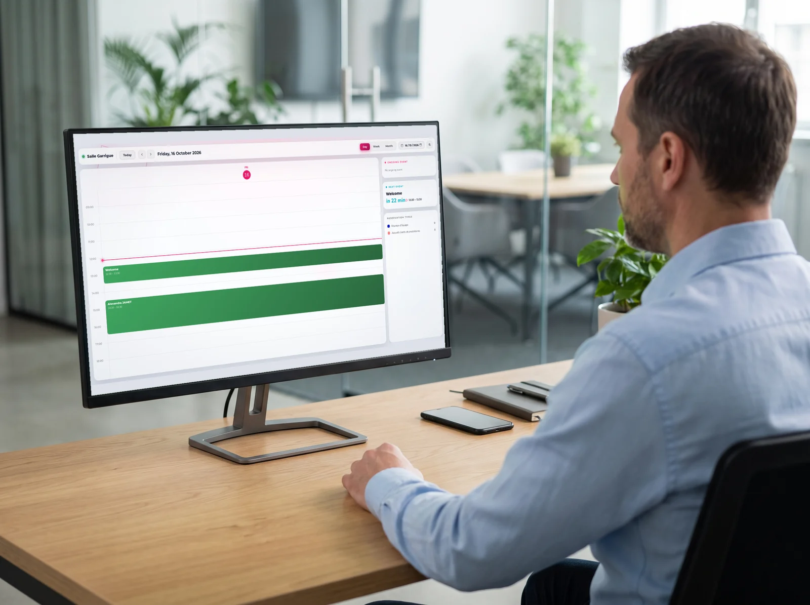 Employee at his desk checking a meeting room calendar in E-MANAGER on his monitor