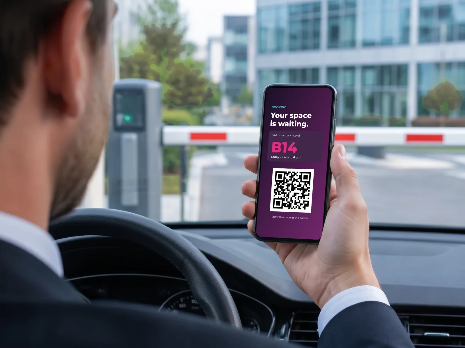 Driver at a car park barrier, smartphone in hand with his reserved space