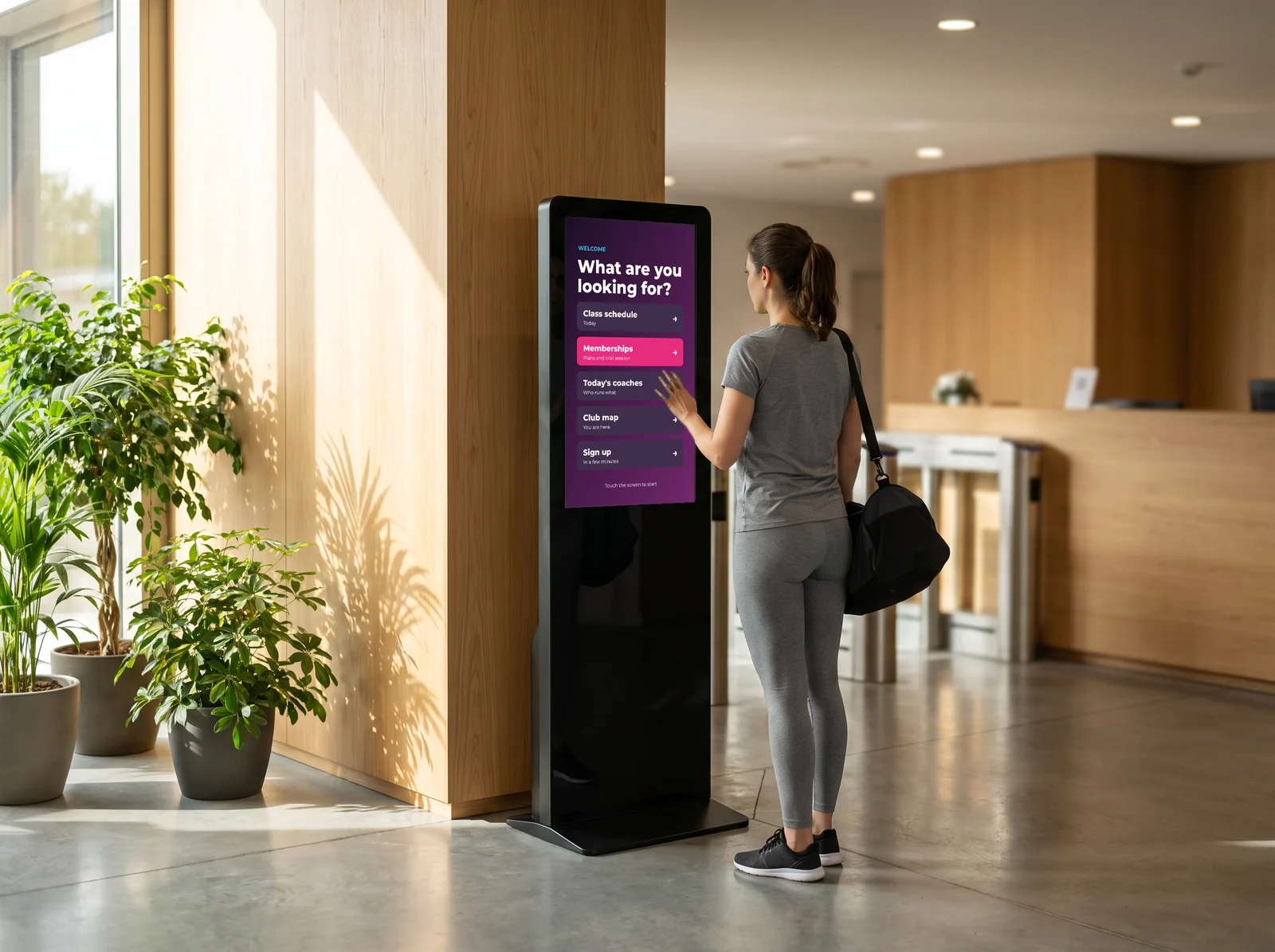 Member using the club's touch kiosk: class schedule, memberships, today's coaches, club map