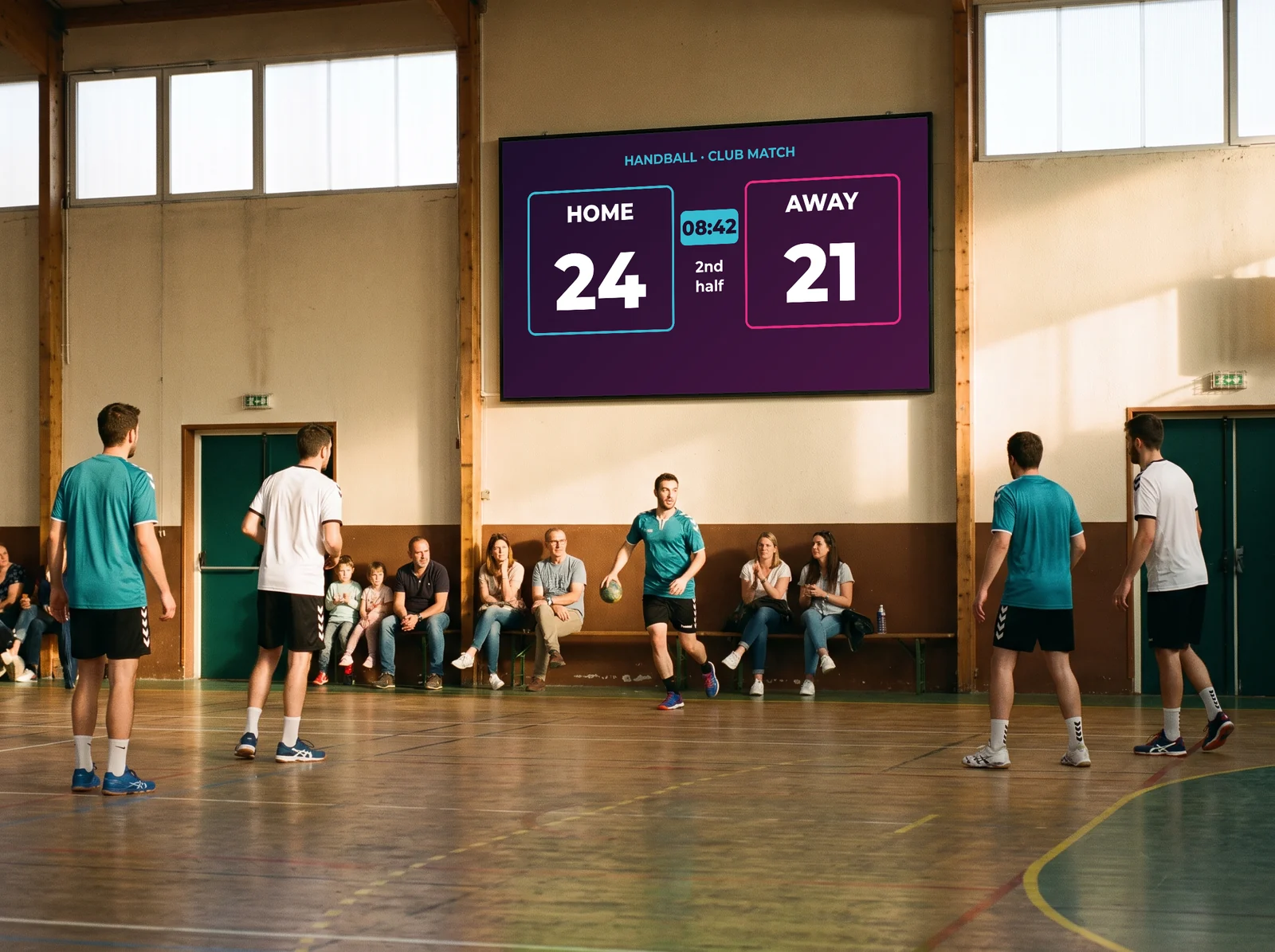 Club handball match in the sports hall: the wall screen shows the live score and the clock