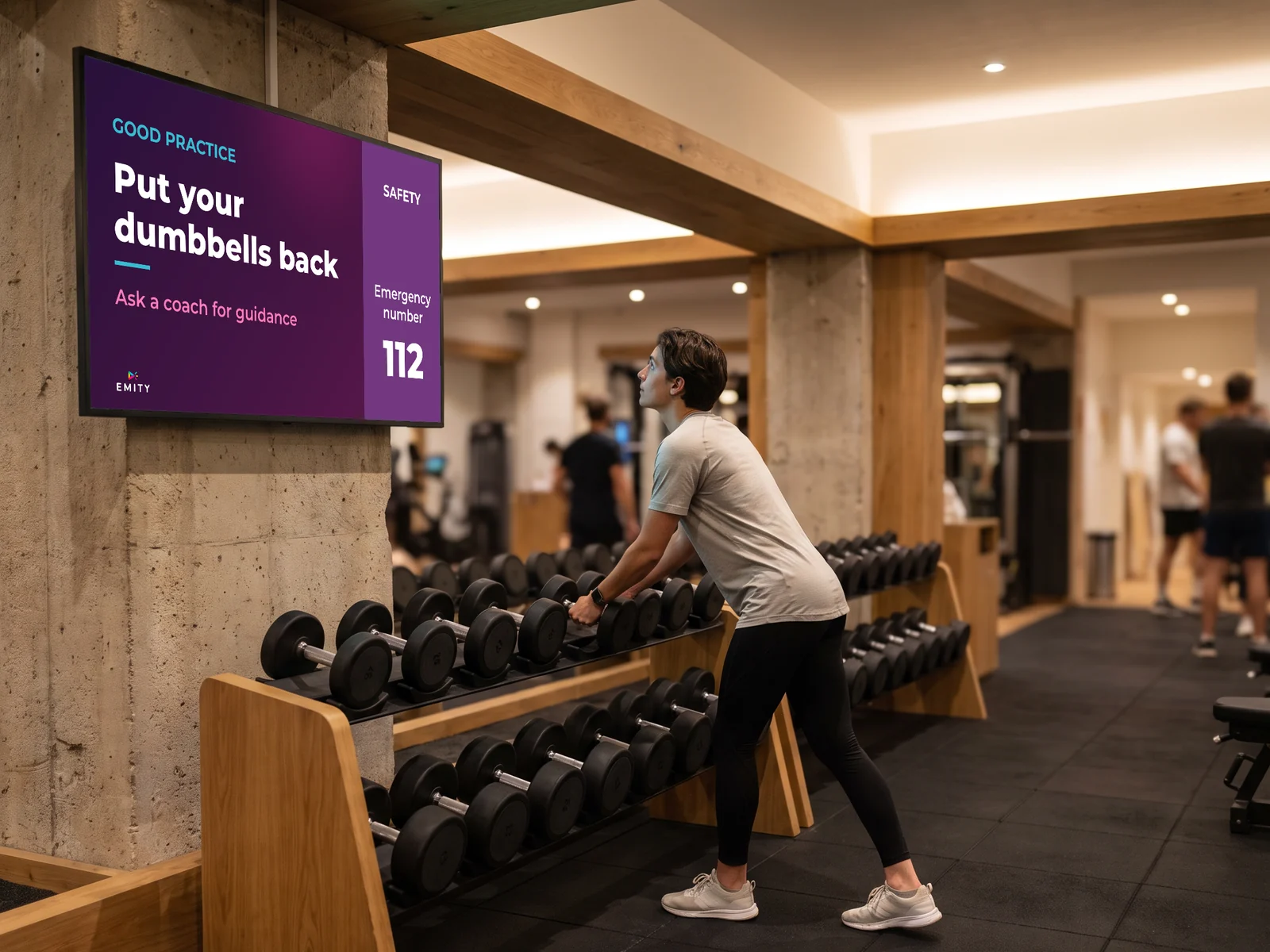 Free weights area: the screen reminds members to put equipment back and shows the emergency number