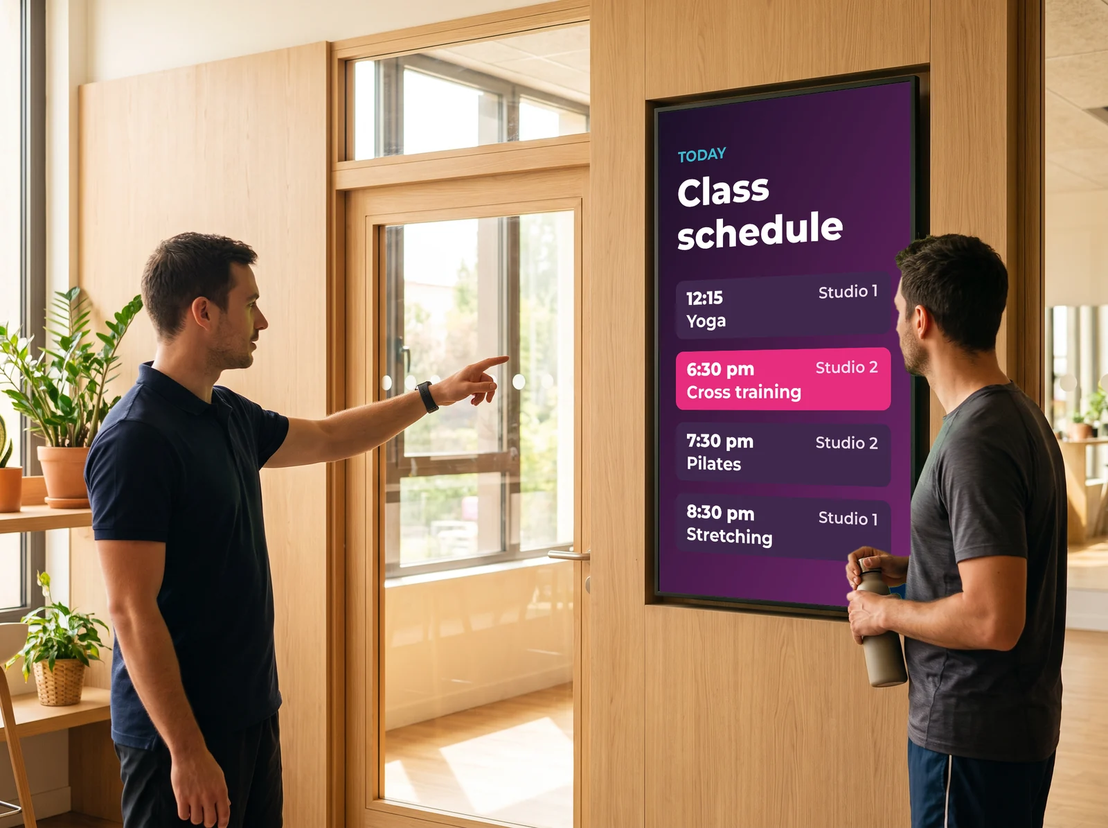 Coach pointing a member to the studio in front of the screen showing today's class schedule