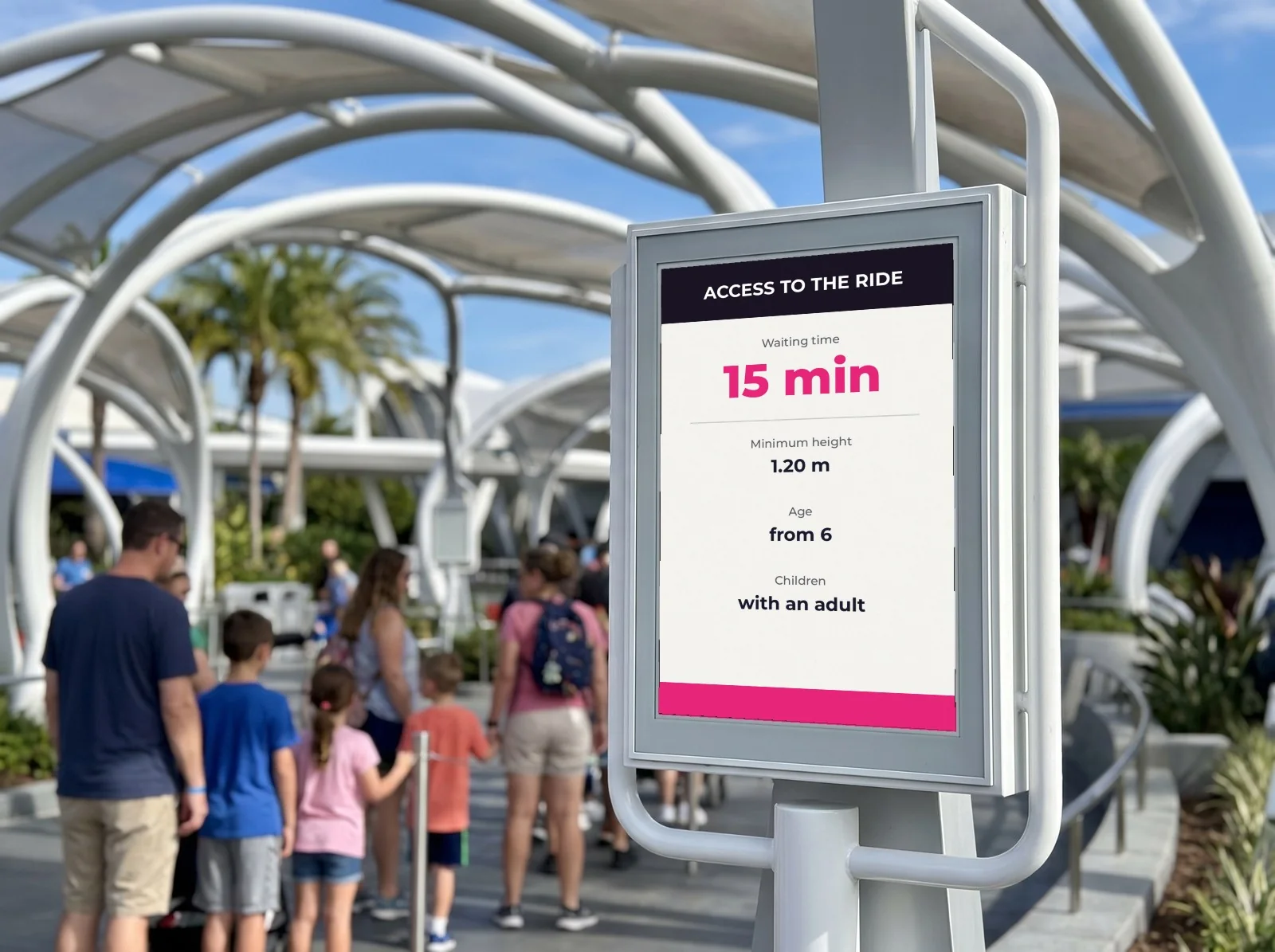 Family queueing at the entrance to a ride, in front of an e-paper sign showing the waiting time