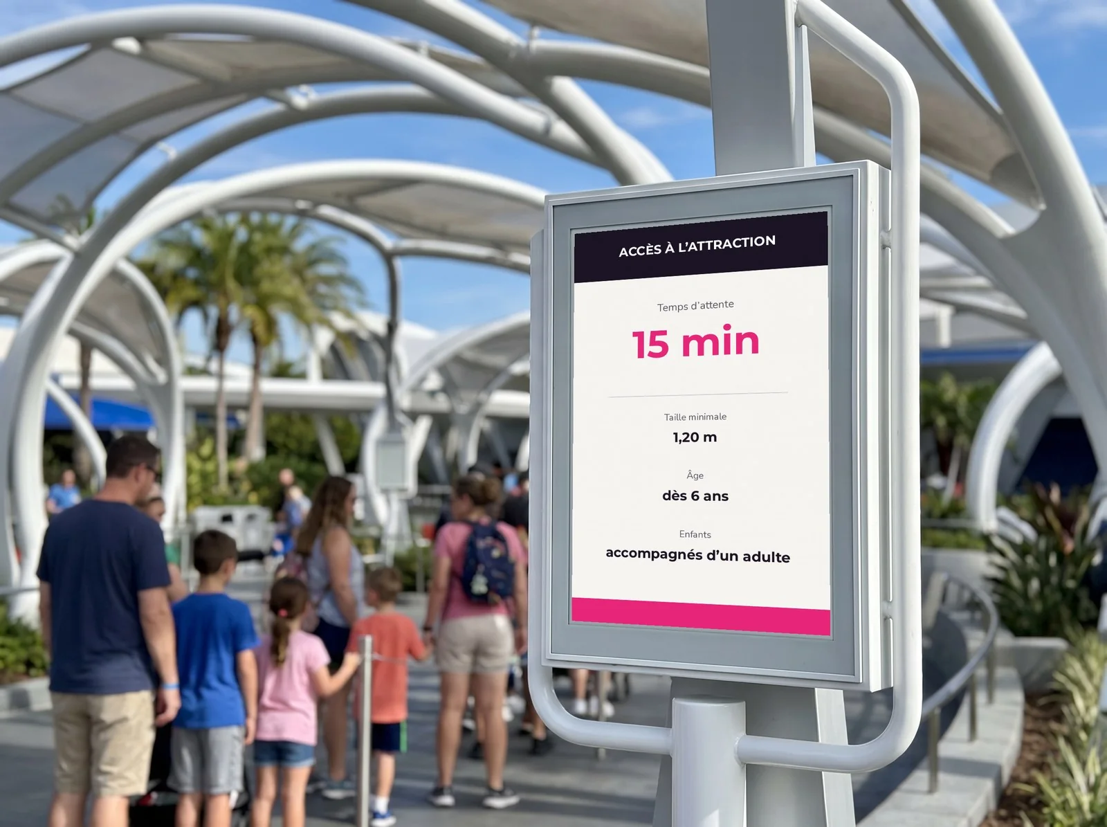 Famille qui fait la queue à l'entrée d'une attraction, devant un panneau e-paper qui affiche le temps d'attente